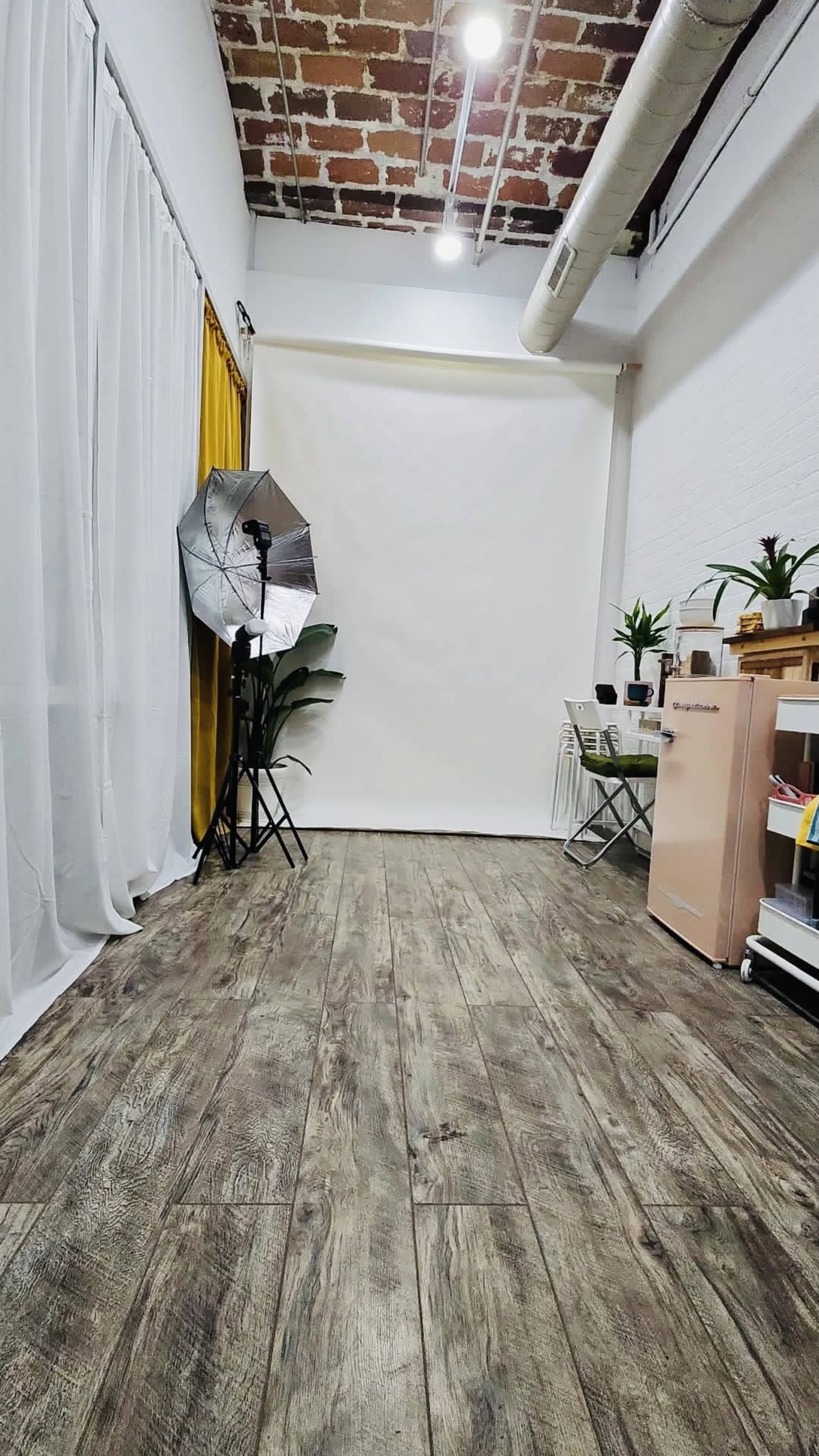 A photography studio with a backdrop, lighting equipment, and simple furniture against a brick and white wall.