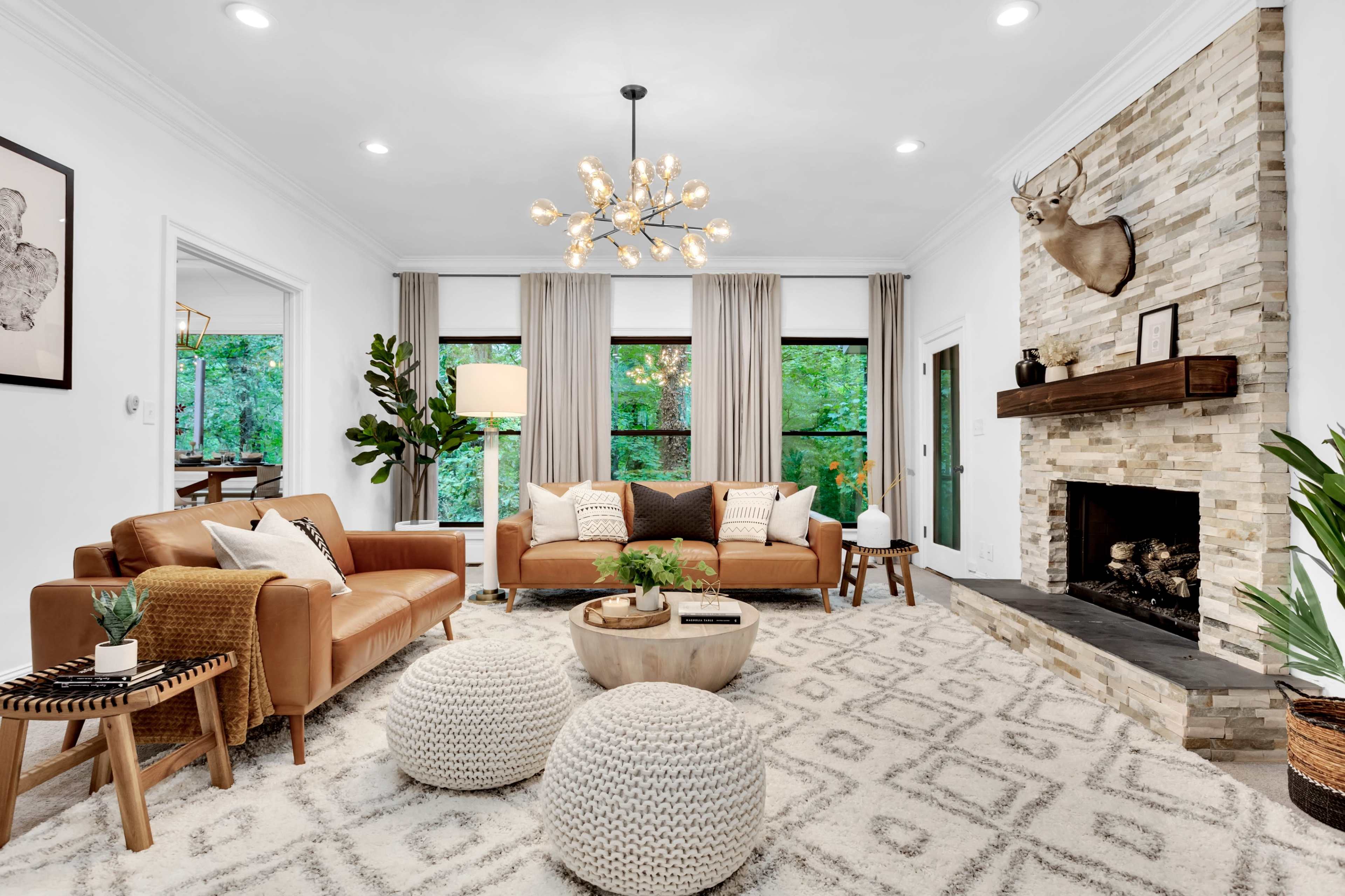 A cozy living room features a stone fireplace, modern furniture, and large windows that overlook greenery.