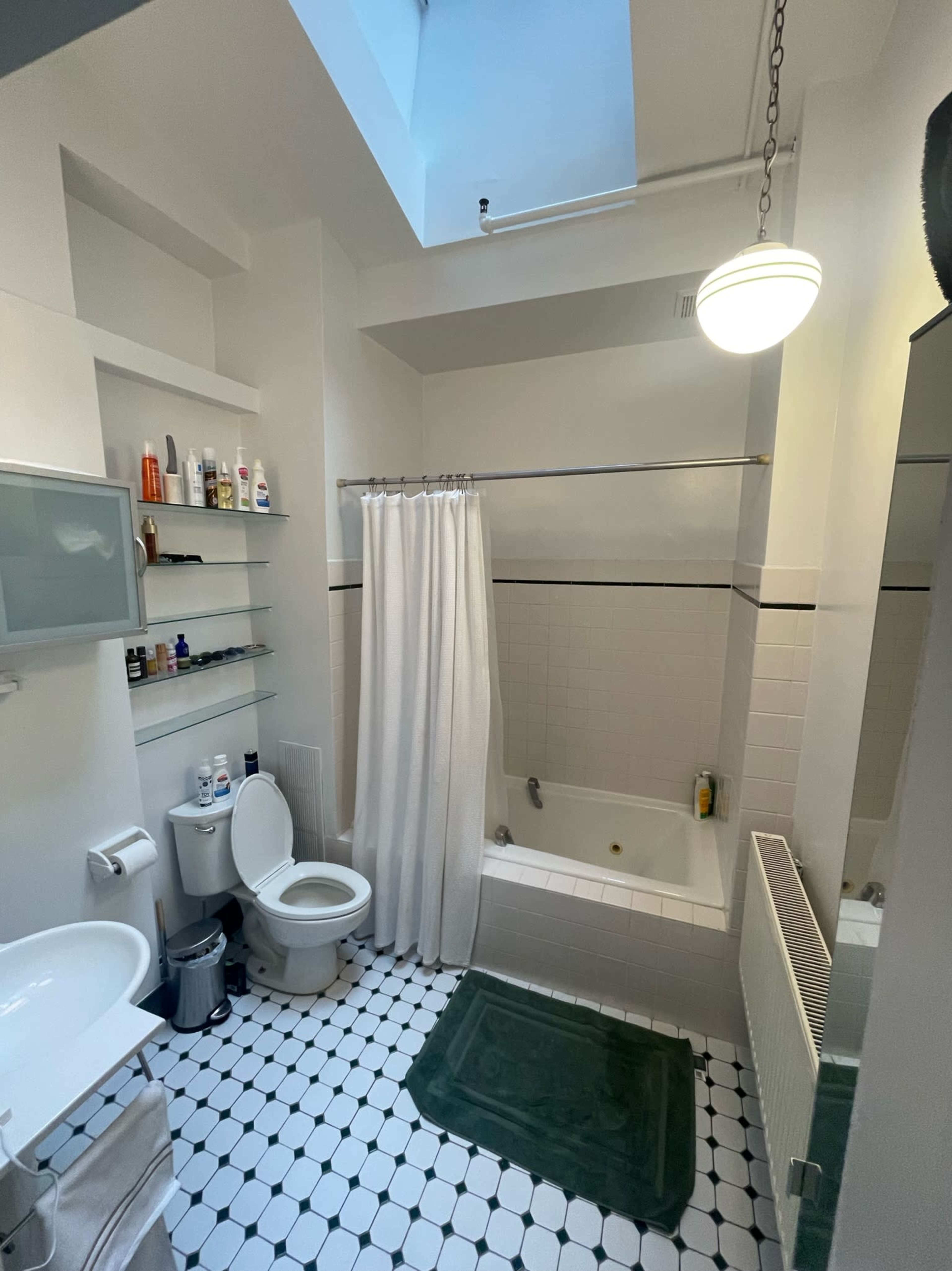 The bathroom features a bathtub with a shower curtain, a toilet, a sink, and shelves with various toiletries.