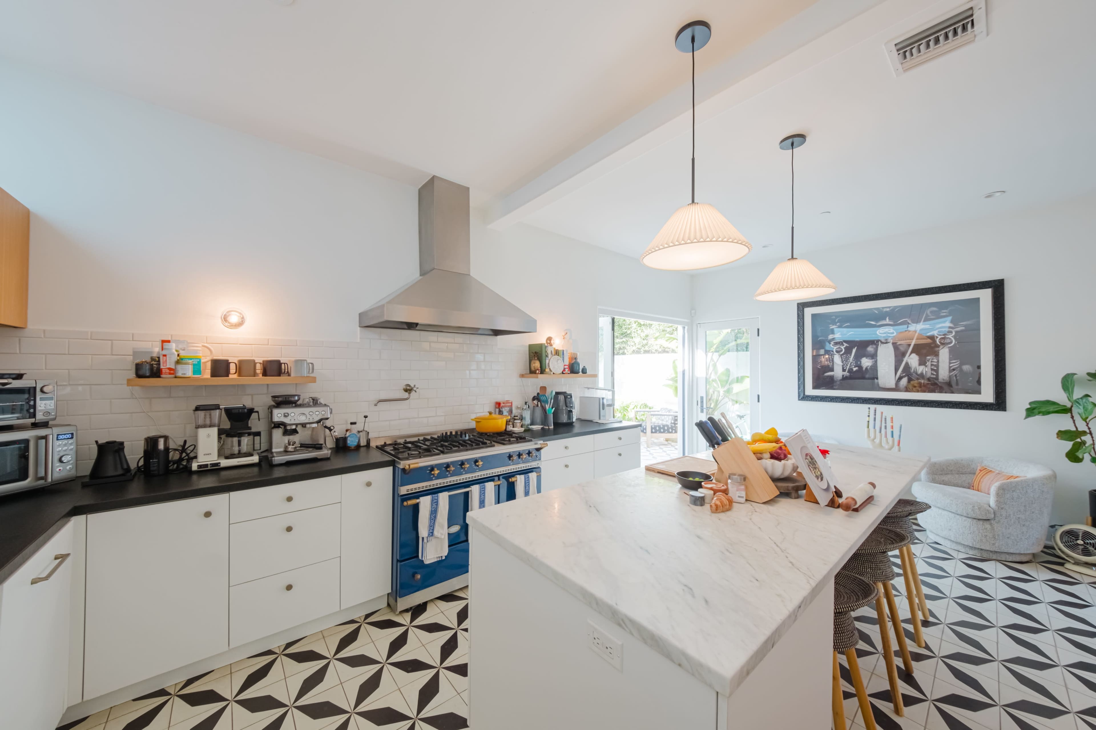 A modern kitchen features a blue stove, stainless steel appliances, marble countertops, and patterned floor tiles.