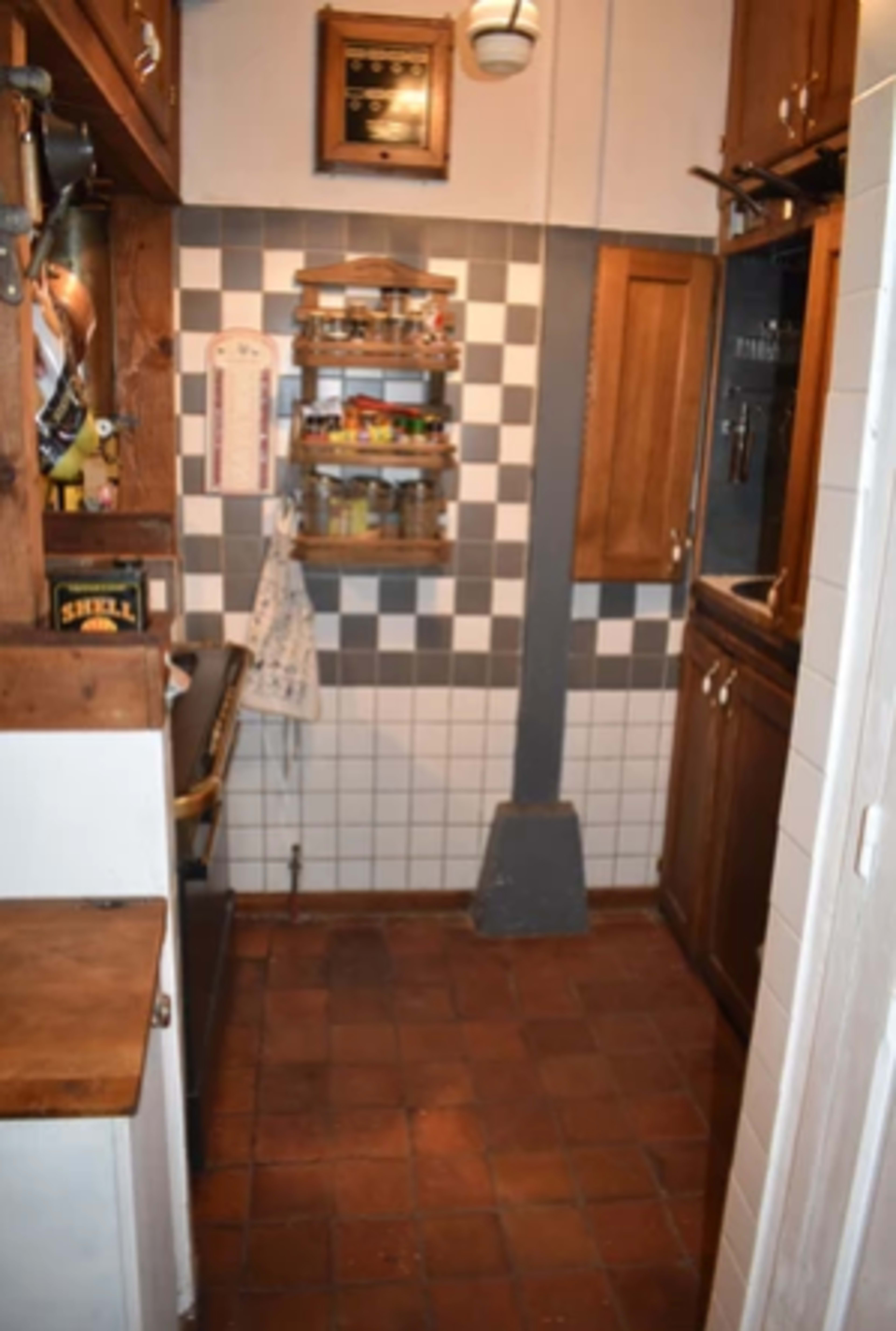 A rectangular kitchen with tiled floors, wooden cabinets, and a wall shelf displaying various jars and spices.