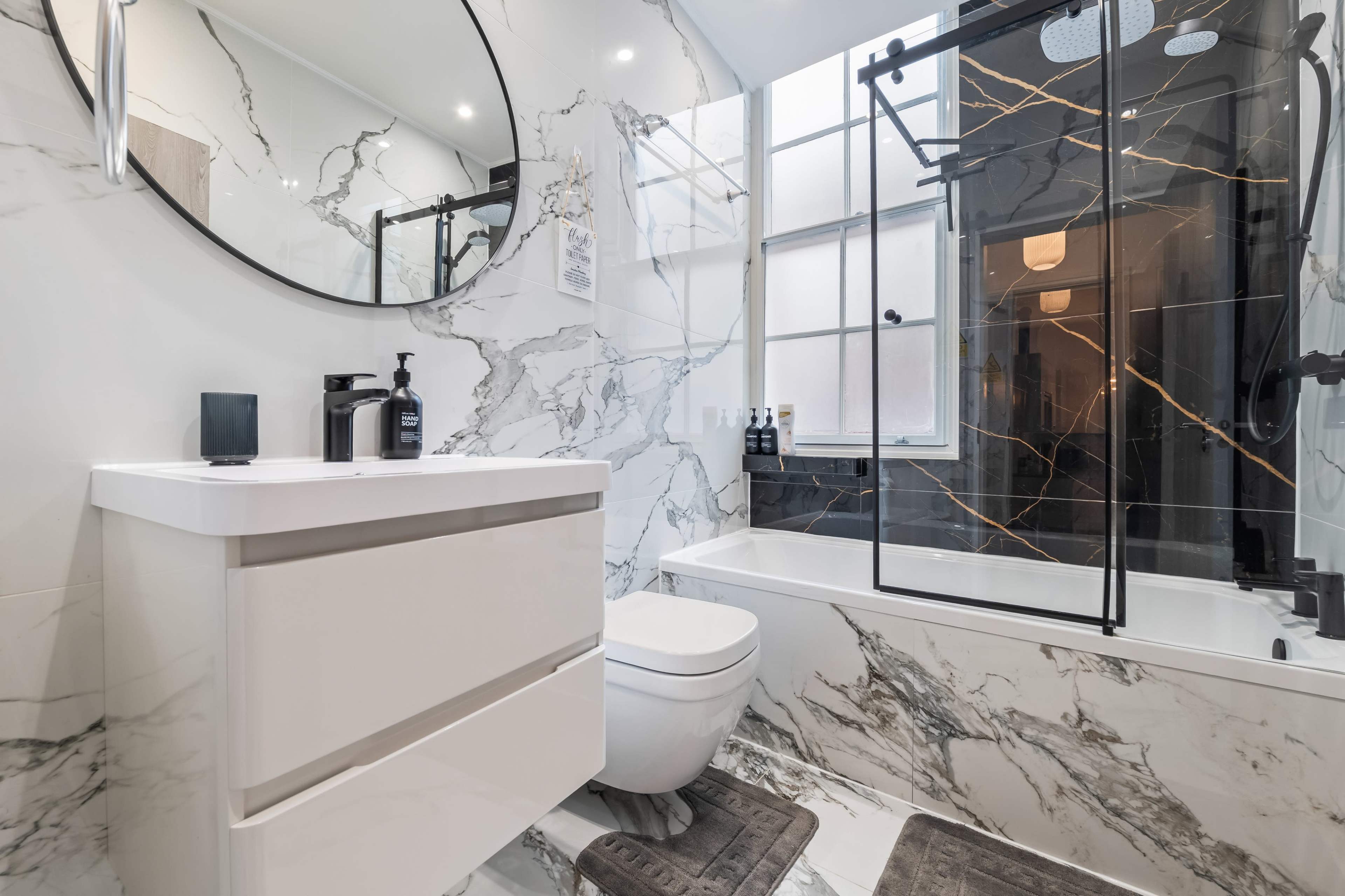 The image shows a modern bathroom featuring a marble-patterned design, a white vanity with a mirror, a glass shower enclosure, and a bathtub.