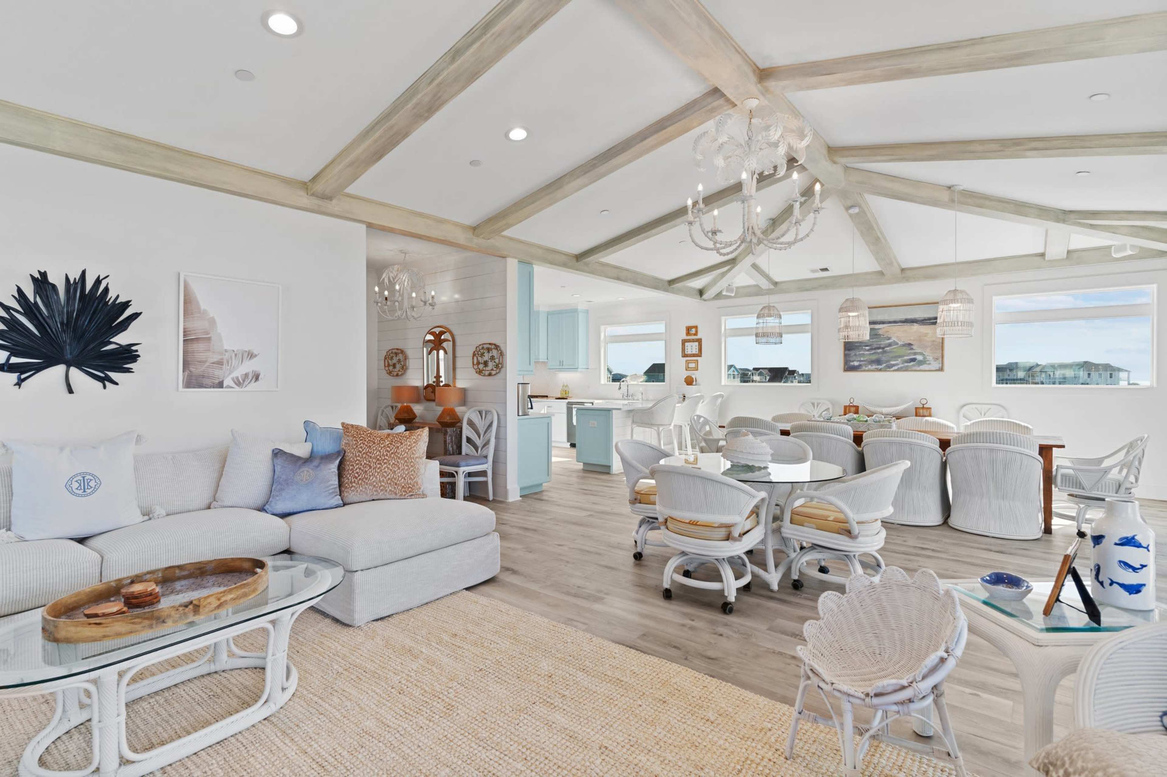 A bright, open living and dining area featuring a light-colored sectional sofa, a dining table surrounded by white chairs, and large windows that allow natural light to fill the space.