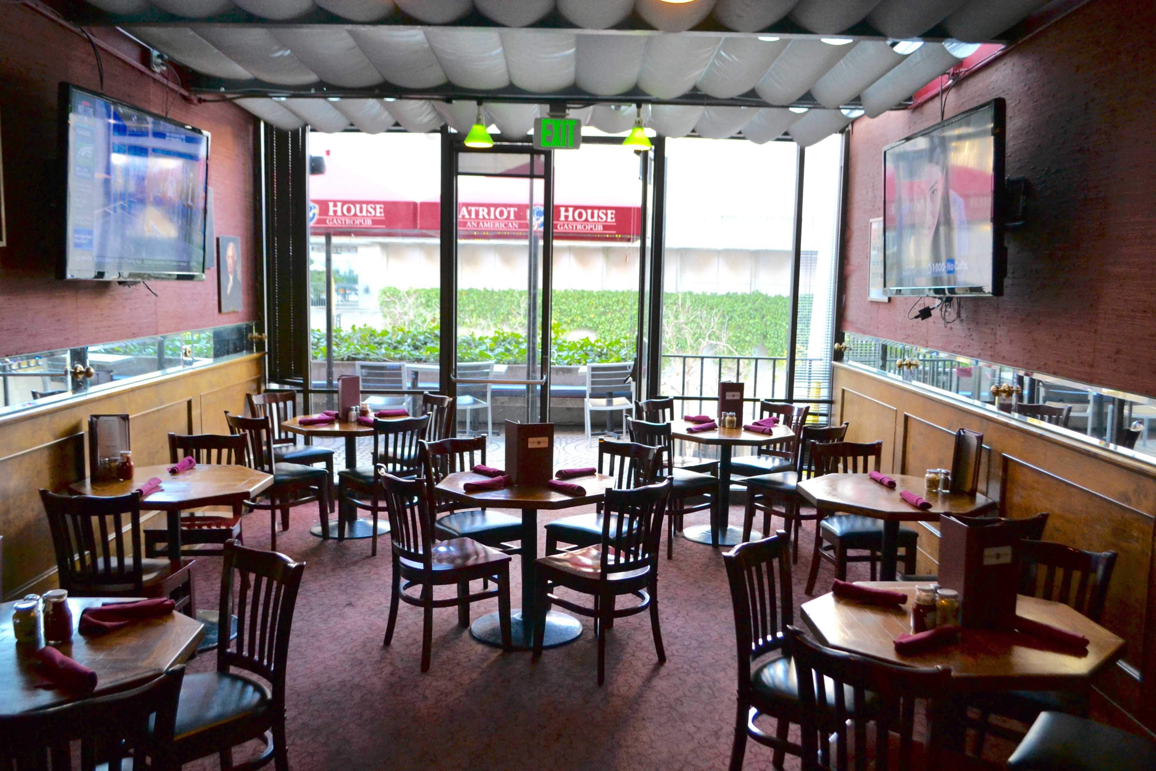 An indoor restaurant with wooden tables and chairs arranged neatly, along with two large TVs mounted on the walls.