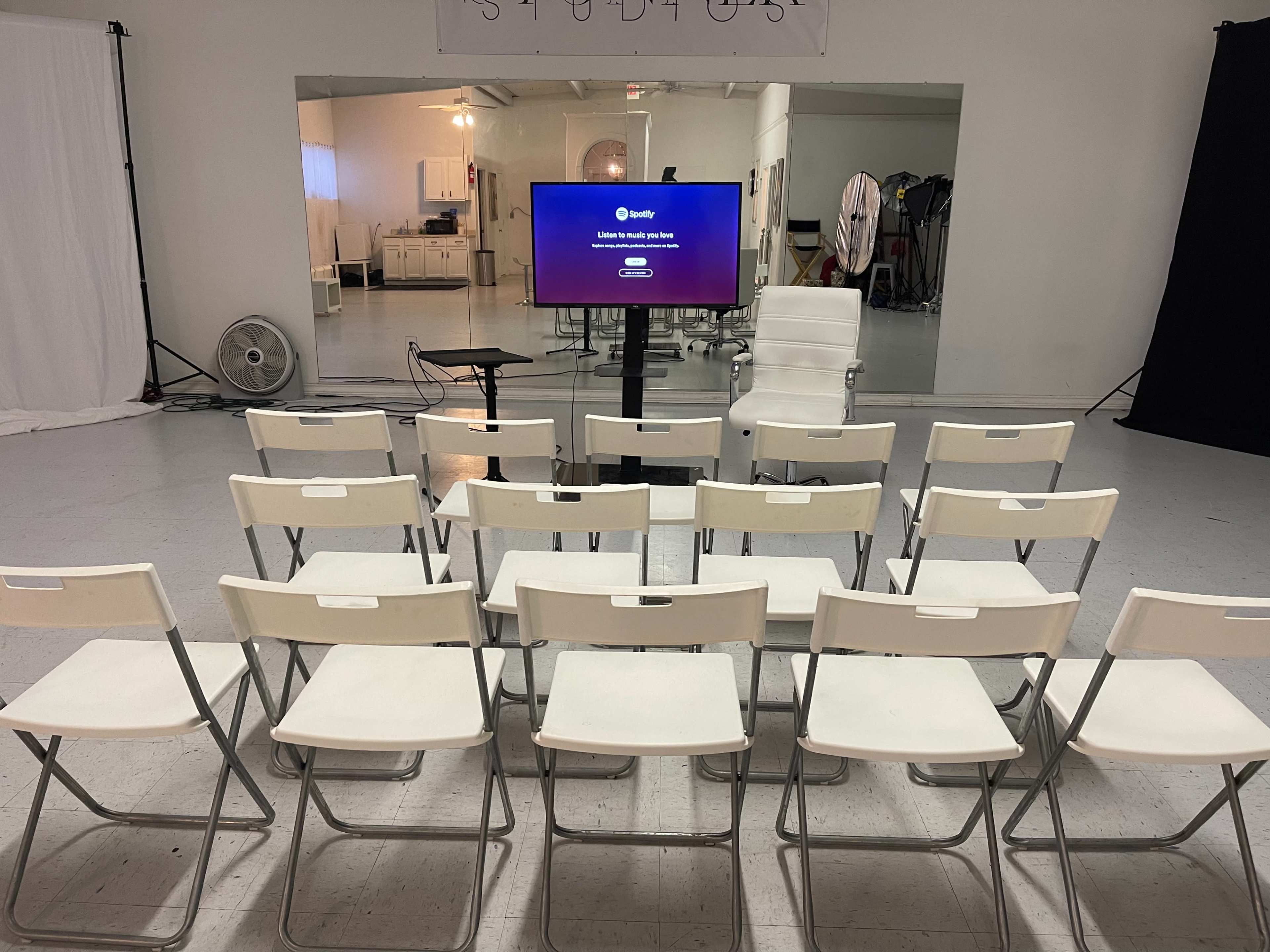 A row of white chairs is arranged facing a television displaying the Spotify logo in a spacious, brightly lit studio.