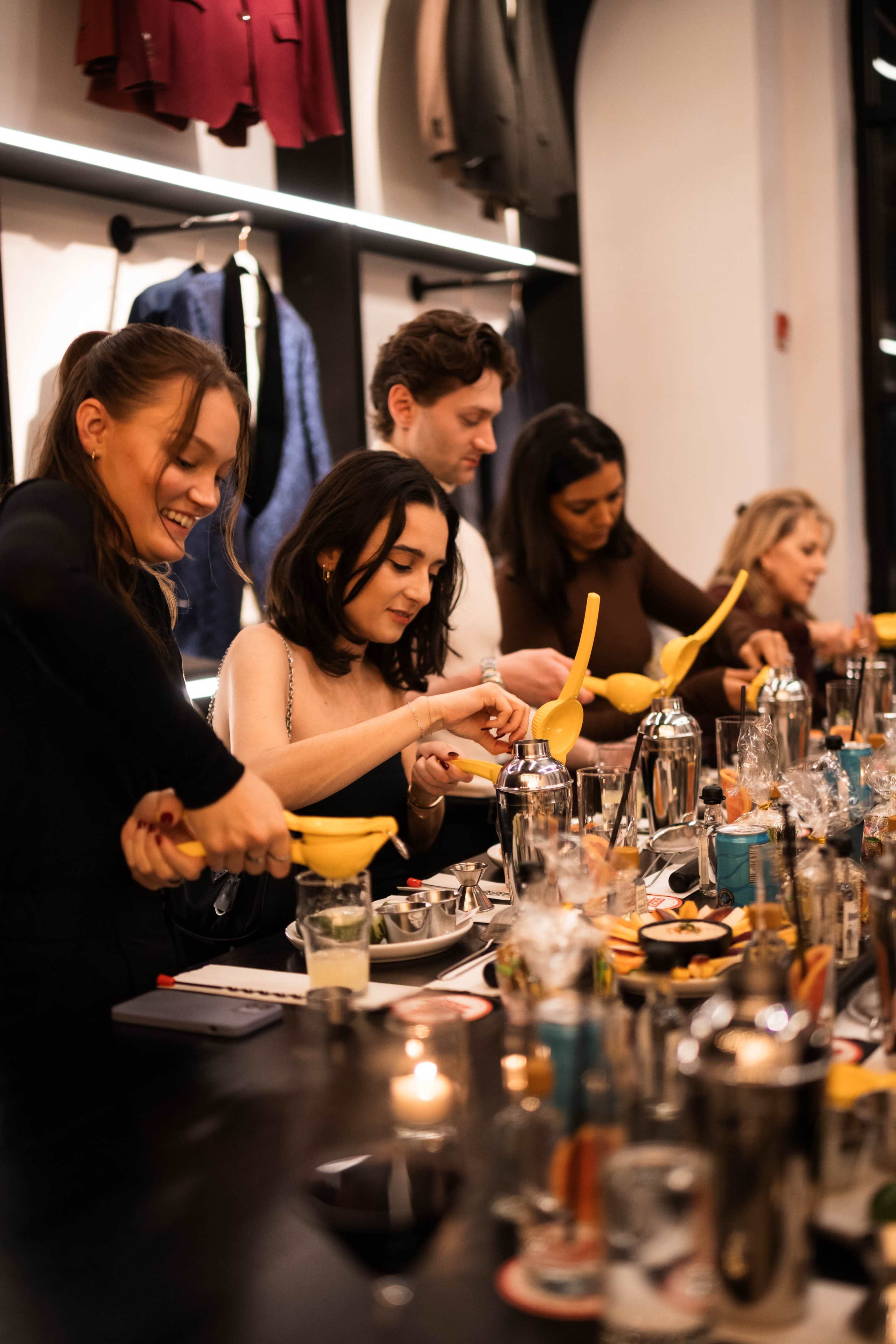 A group of people is engaged in a cocktail-making activity at a long table filled with various drink ingredients and tools.