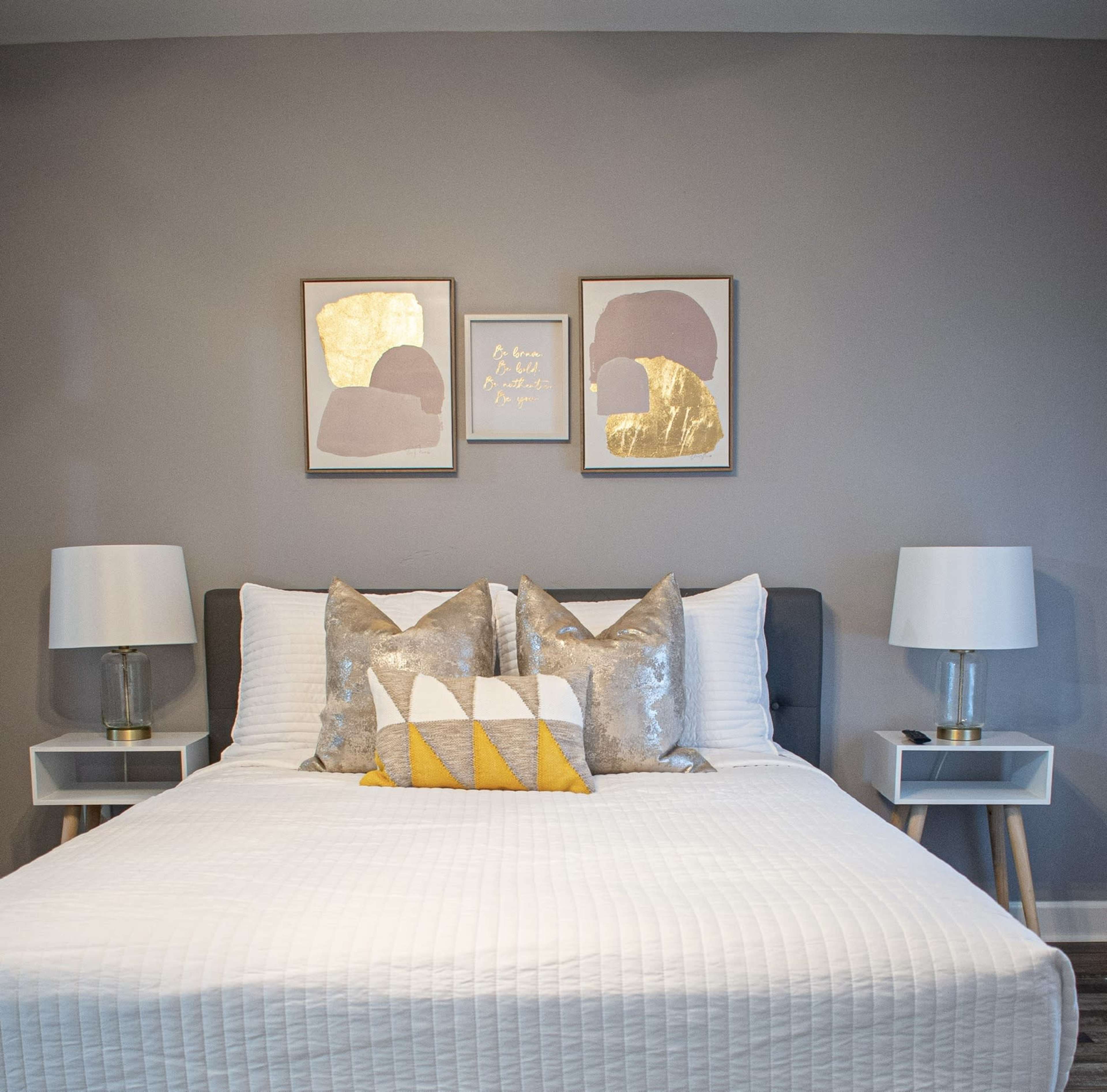 A neatly arranged bedroom featuring a bed with white linens, decorative pillows, and two bedside tables with lamps, along with framed art on the wall.