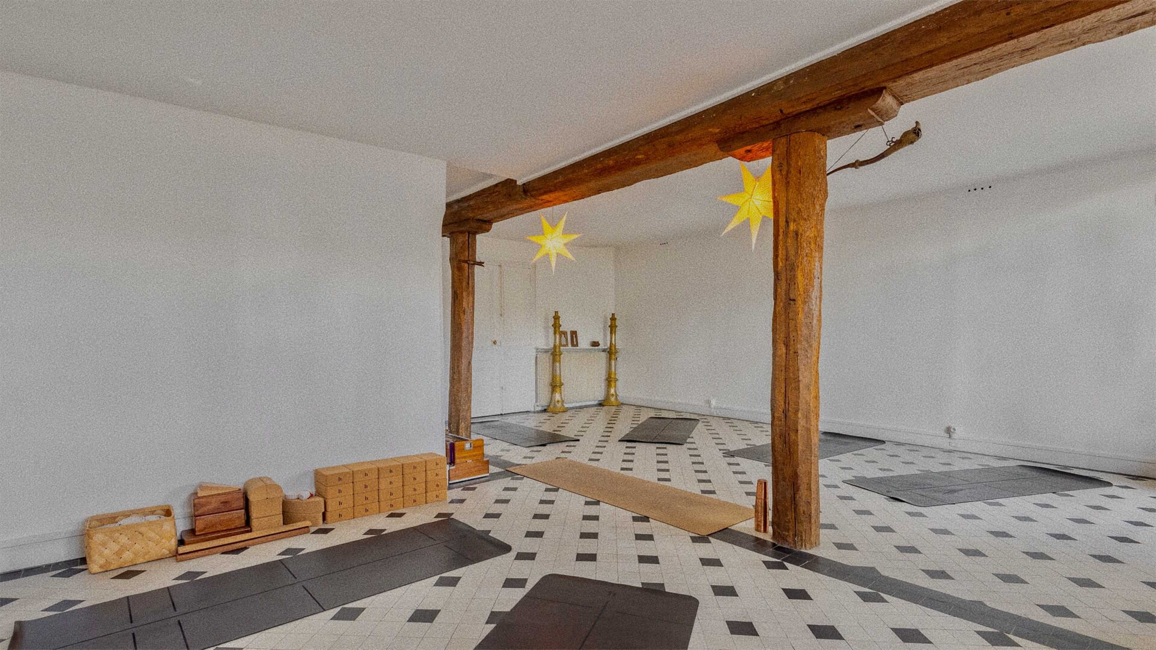 A spacious room with a patterned tiled floor, wooden beams, and a few boxes stacked on one side.