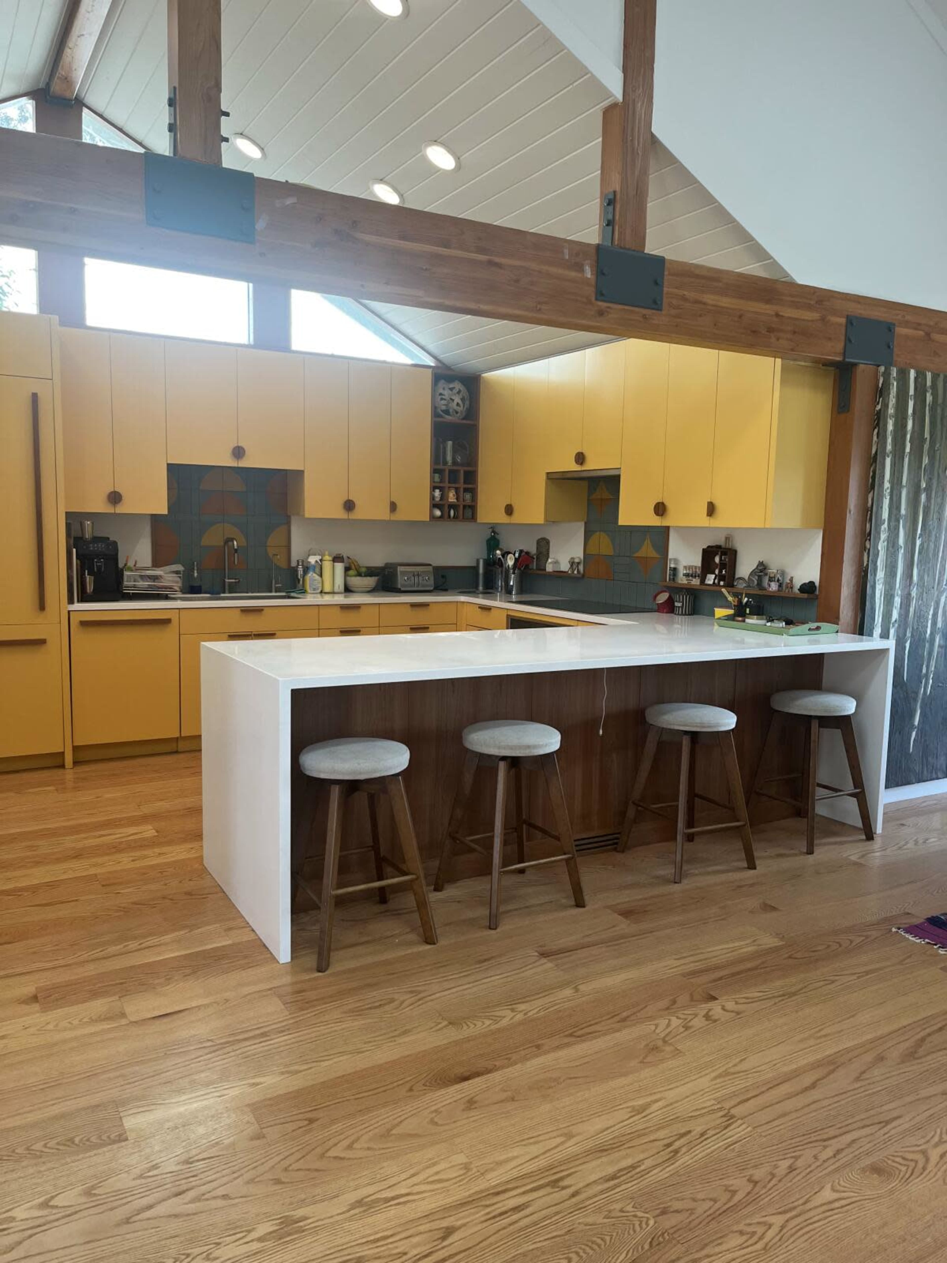 The image shows a modern kitchen featuring yellow cabinetry, a central white island, and wooden bar stools.