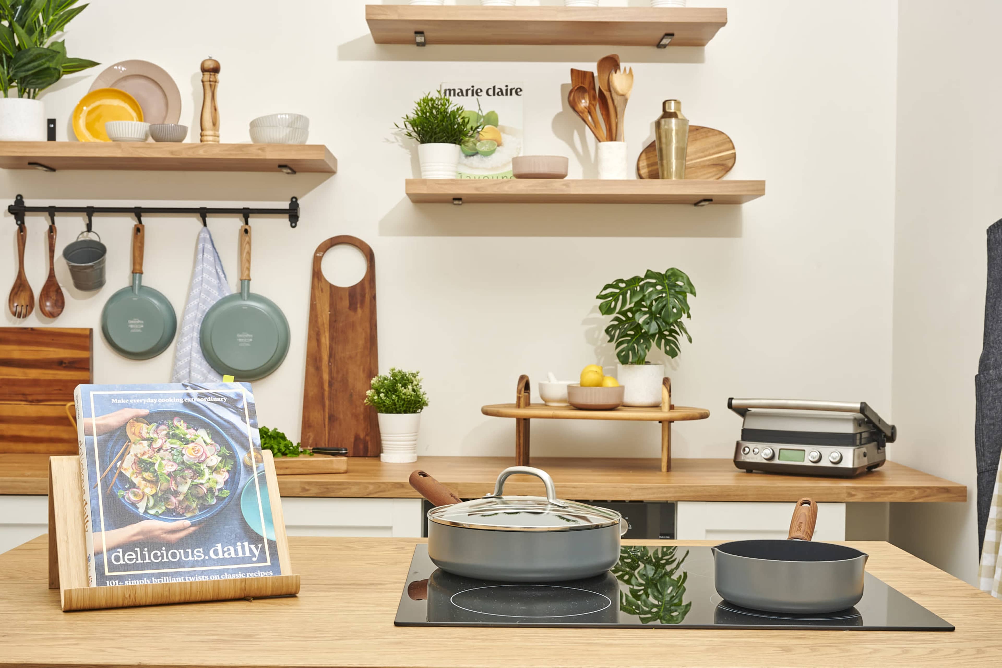 A modern kitchen features wooden shelves with various cooking utensils, pots on a stove, and a cookbook displayed on the counter.