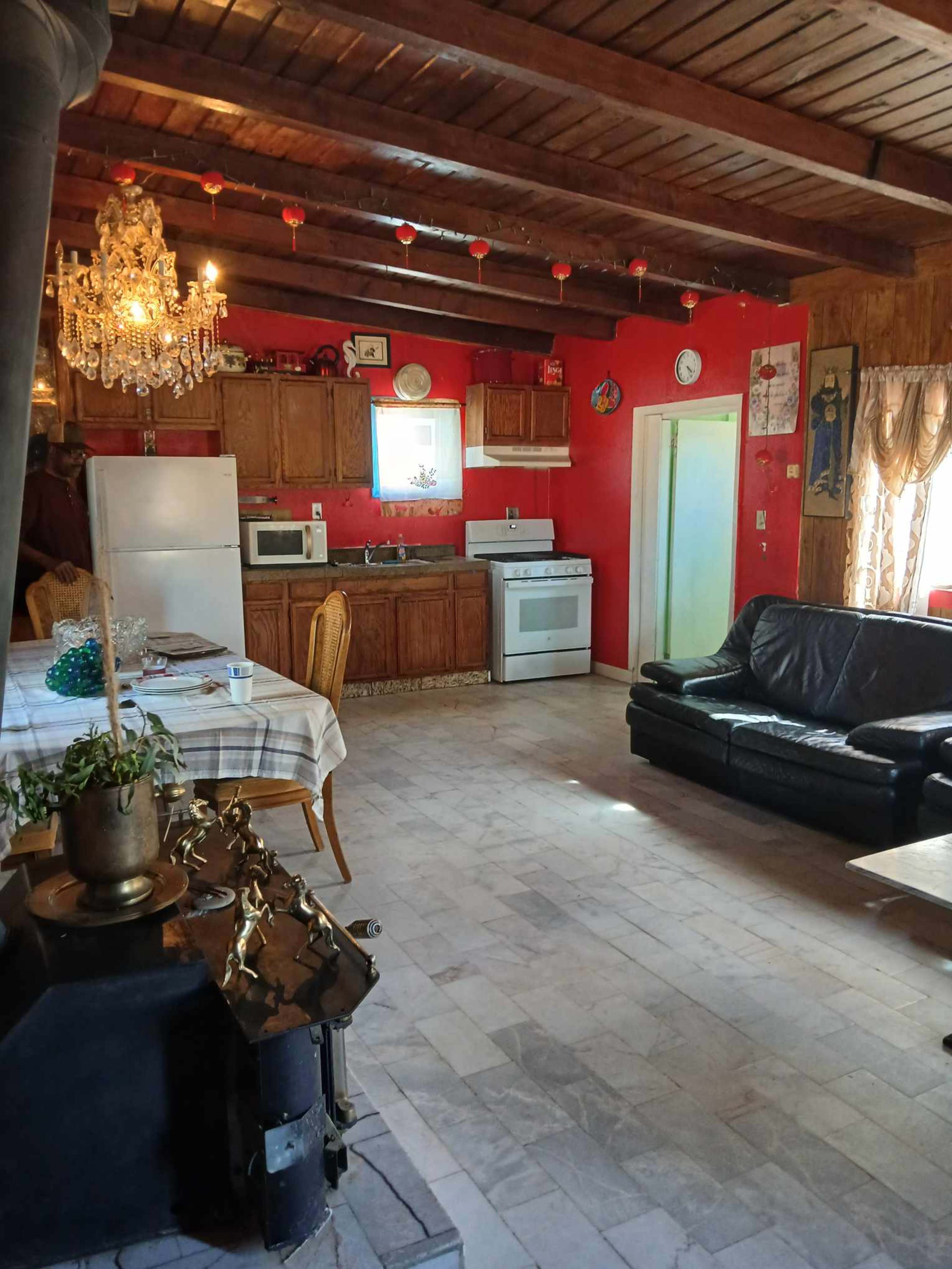The image shows a kitchen and living area with wooden beams, red walls, a chandelier, and a black couch.
