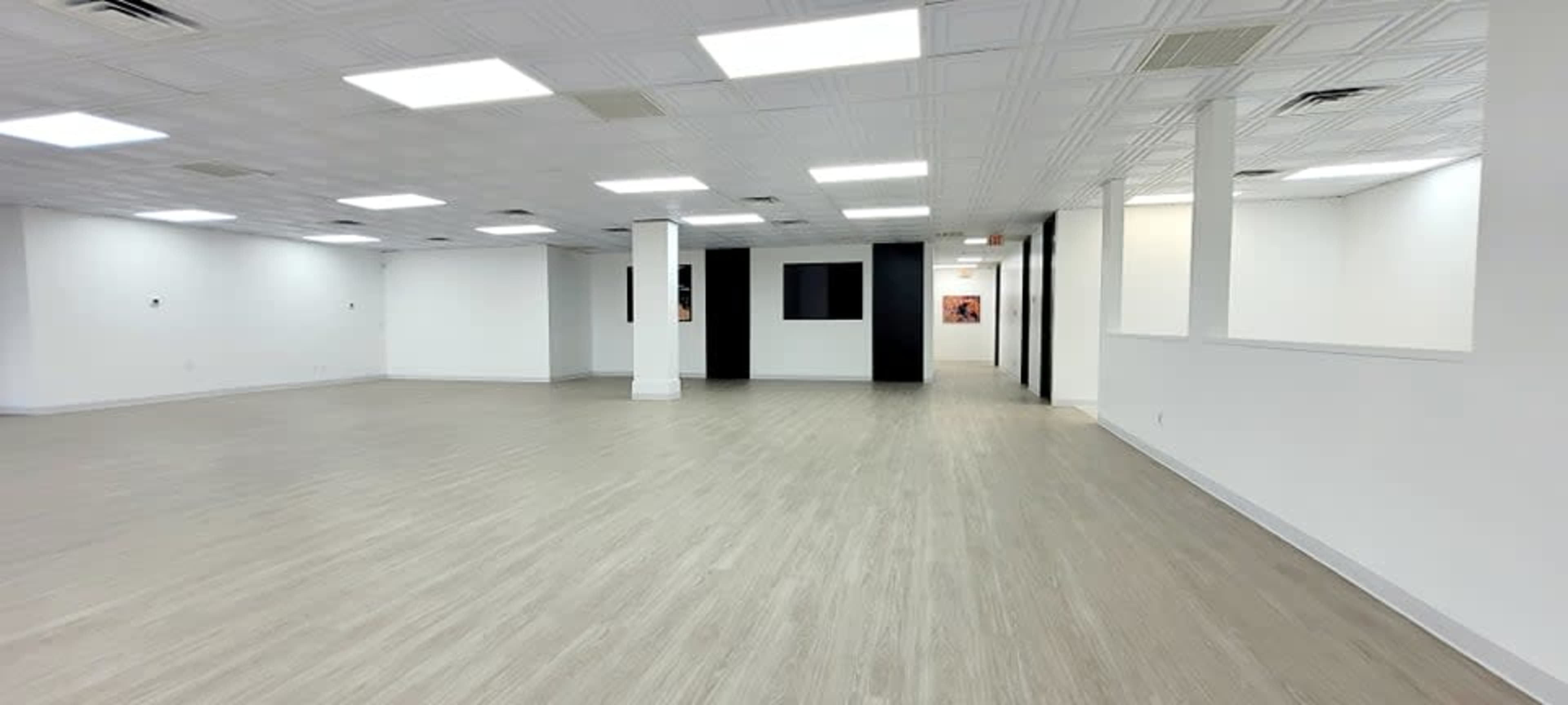 A spacious, empty room with light-colored flooring and white walls, featuring a few partitions and large windows.