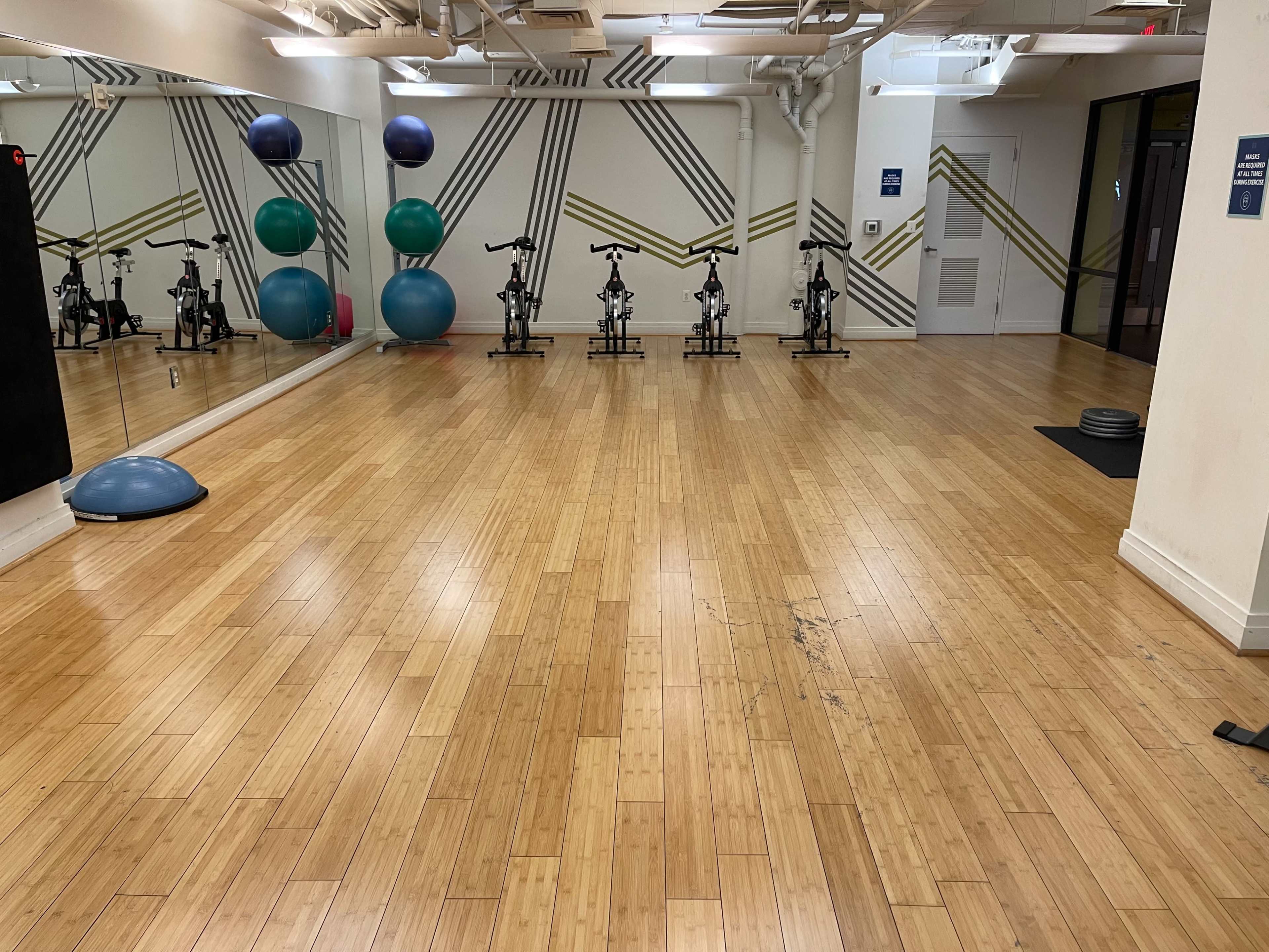 A spacious fitness studio with wooden flooring, exercise bikes lined up against a wall, and various fitness balls placed in the corner.