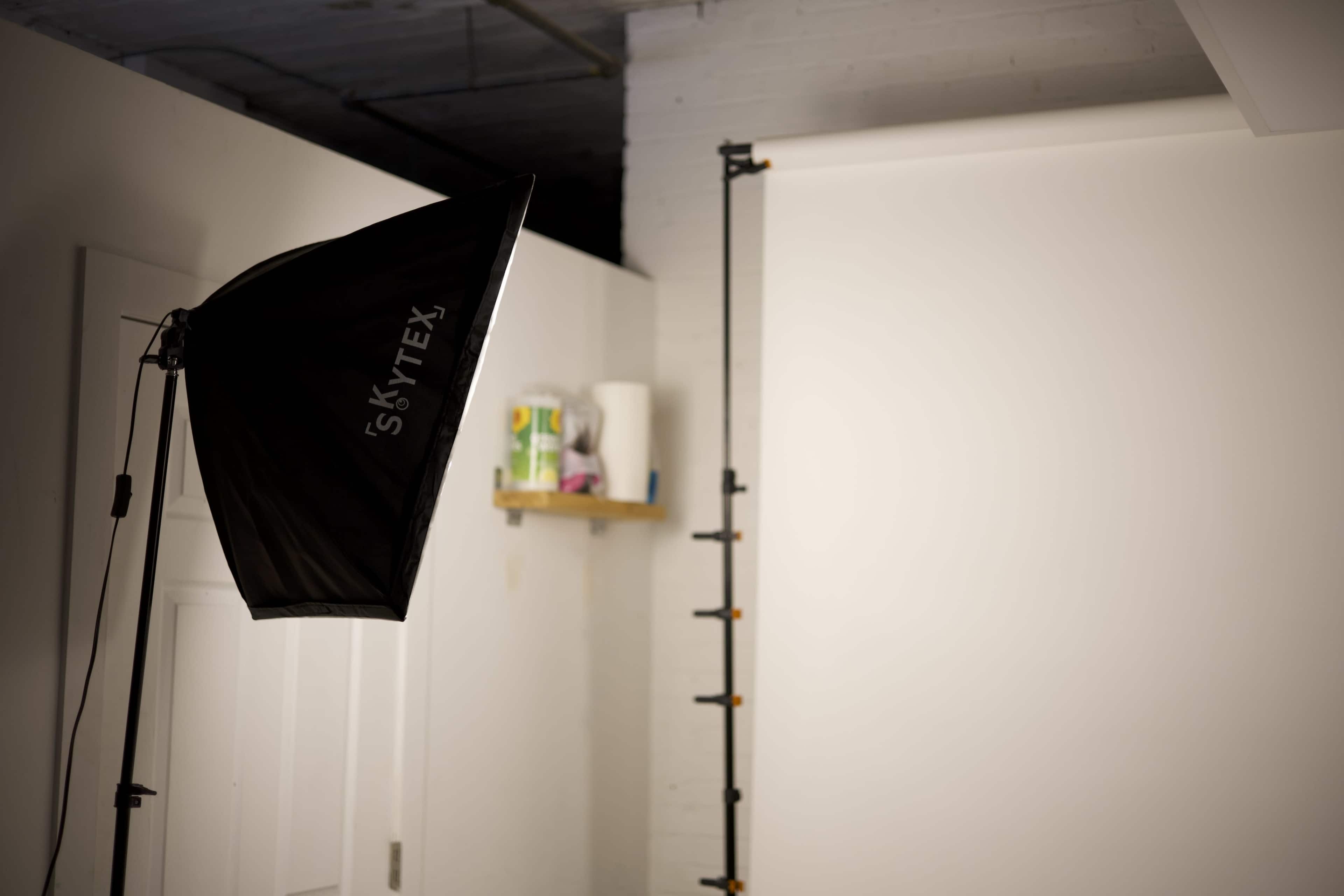 A photography studio setup is shown, featuring a softbox light and a plain backdrop.