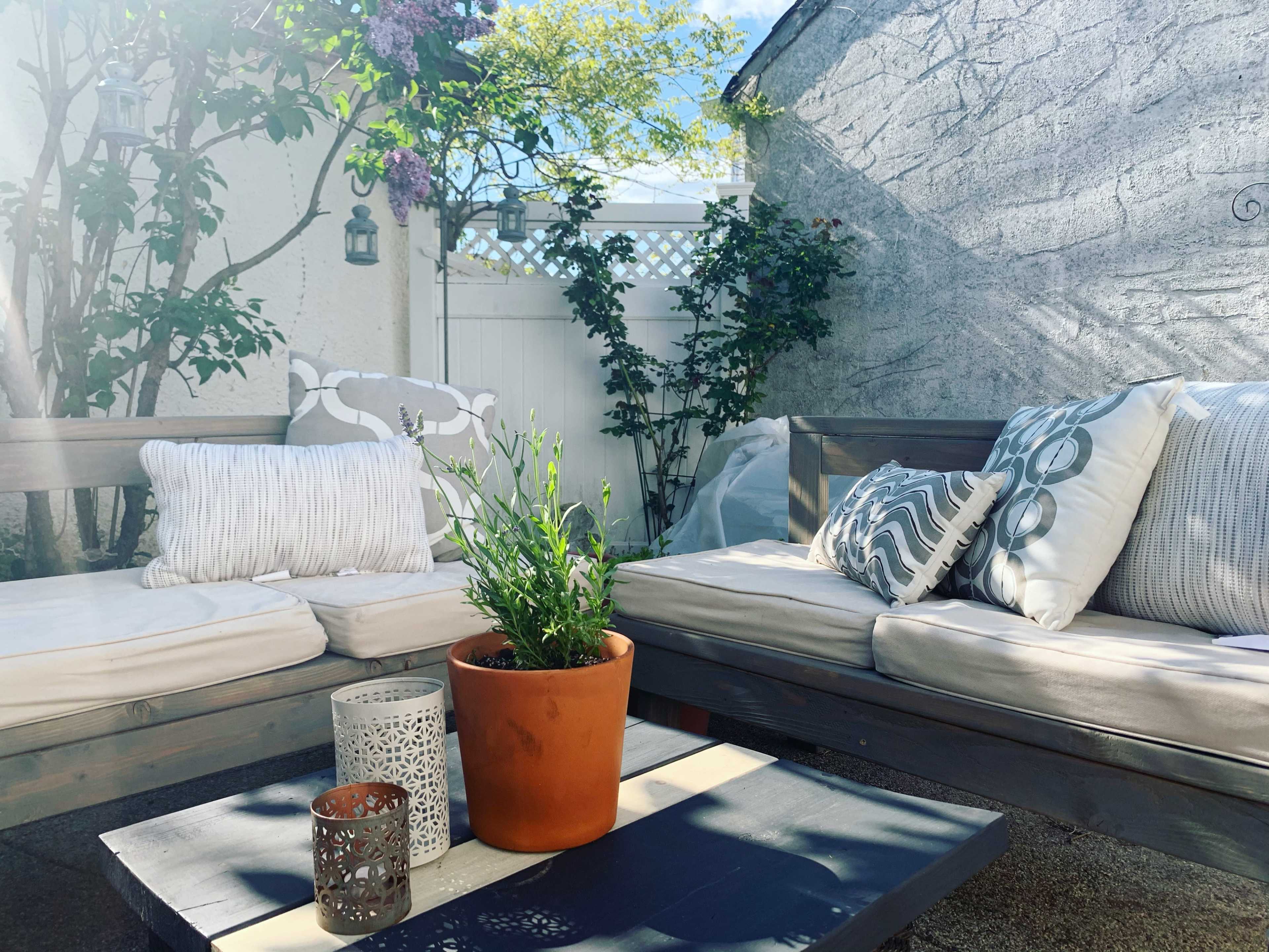 A cozy outdoor seating area features two wooden couches adorned with decorative pillows and a potted plant on a coffee table.