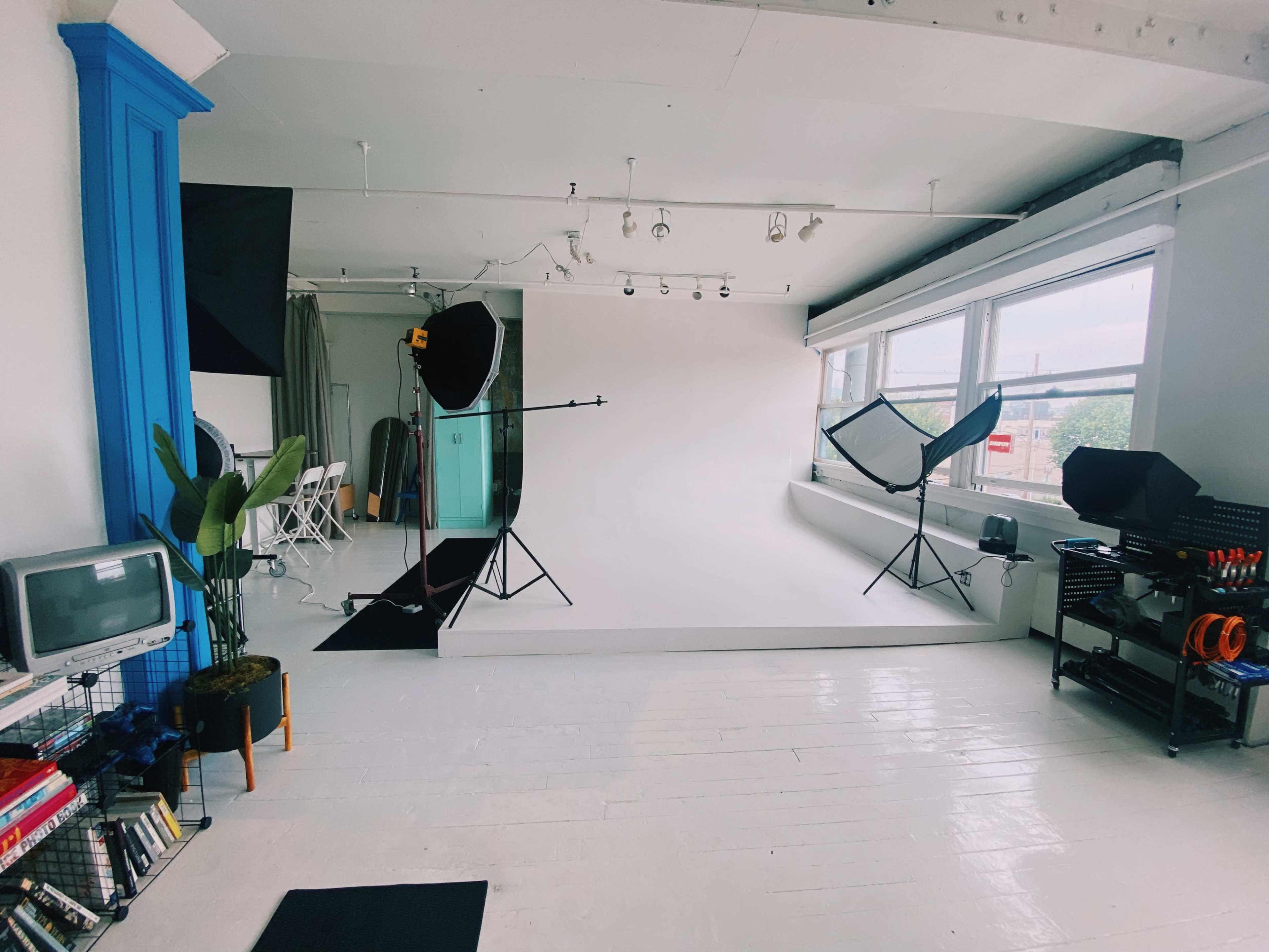 The image shows a photography studio with a white backdrop, lighting equipment, a vintage television, and various shelves filled with items.