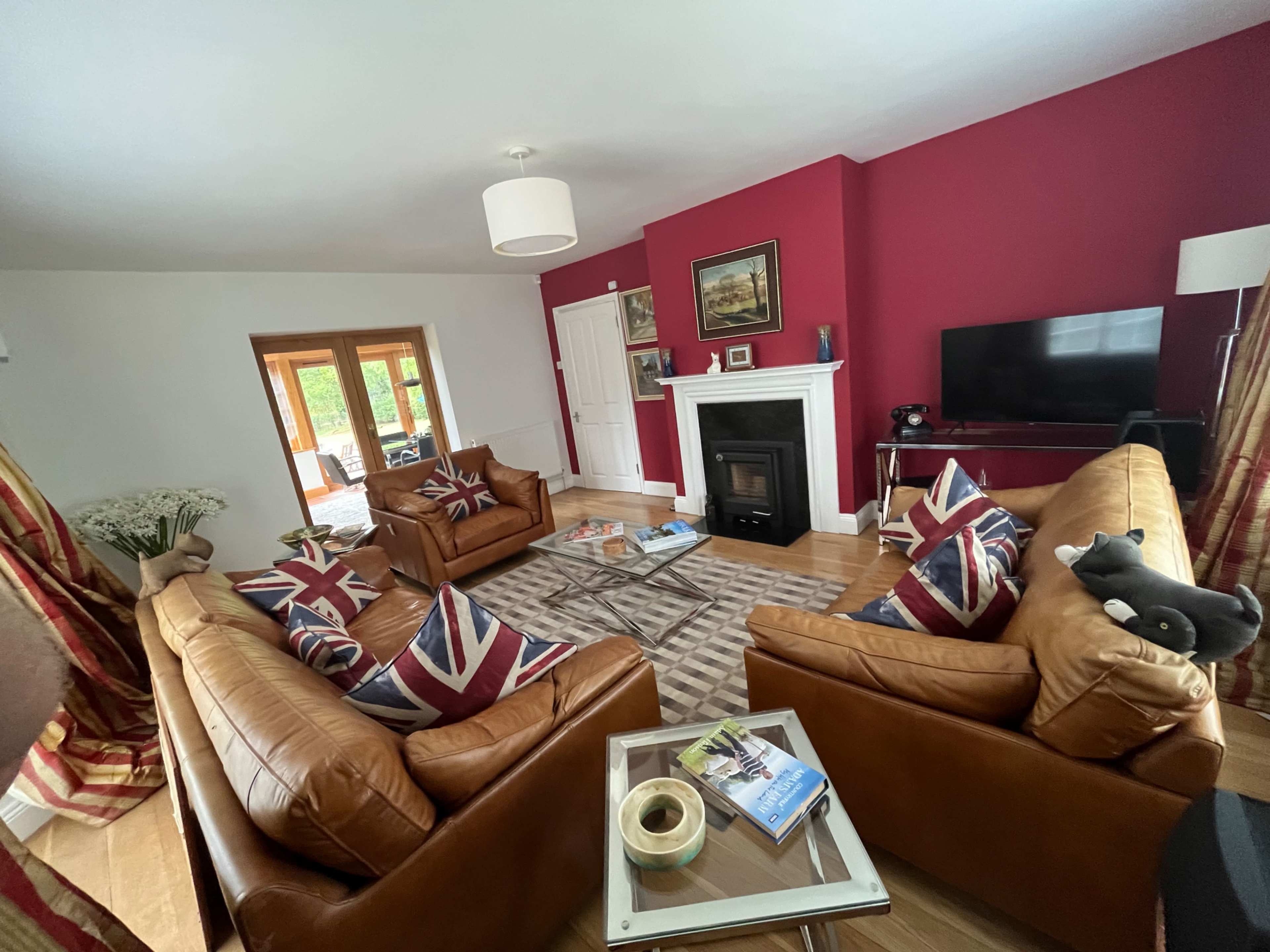 The living room features two brown leather sofas with Union Jack cushions, a coffee table, a fireplace, and a television against a red accent wall.