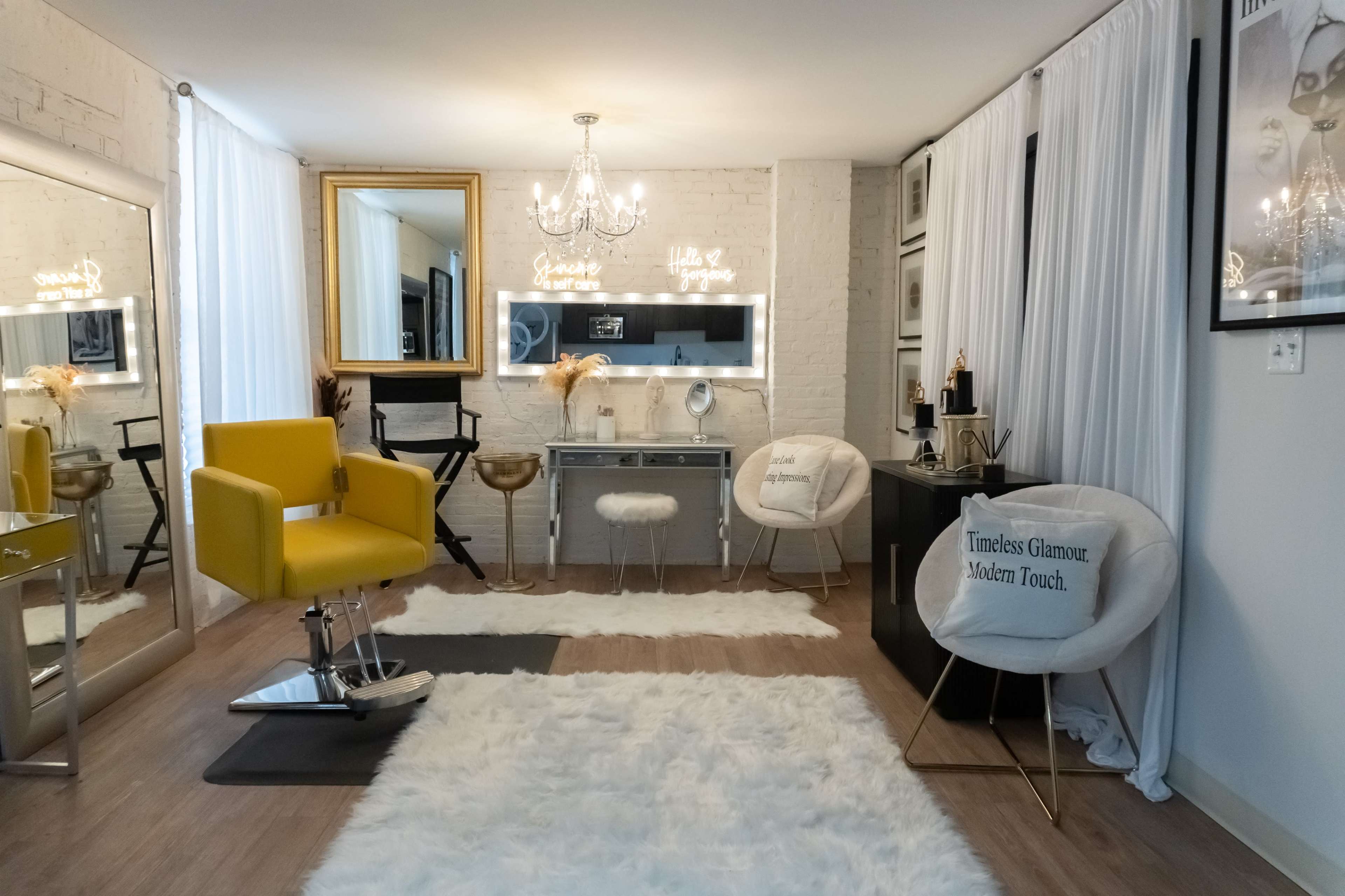 The image shows a modern beauty salon with a bright yellow chair, a mirrored vanity with lights, and stylish seating arrangements, all set against a backdrop of white brick walls and soft carpeting.