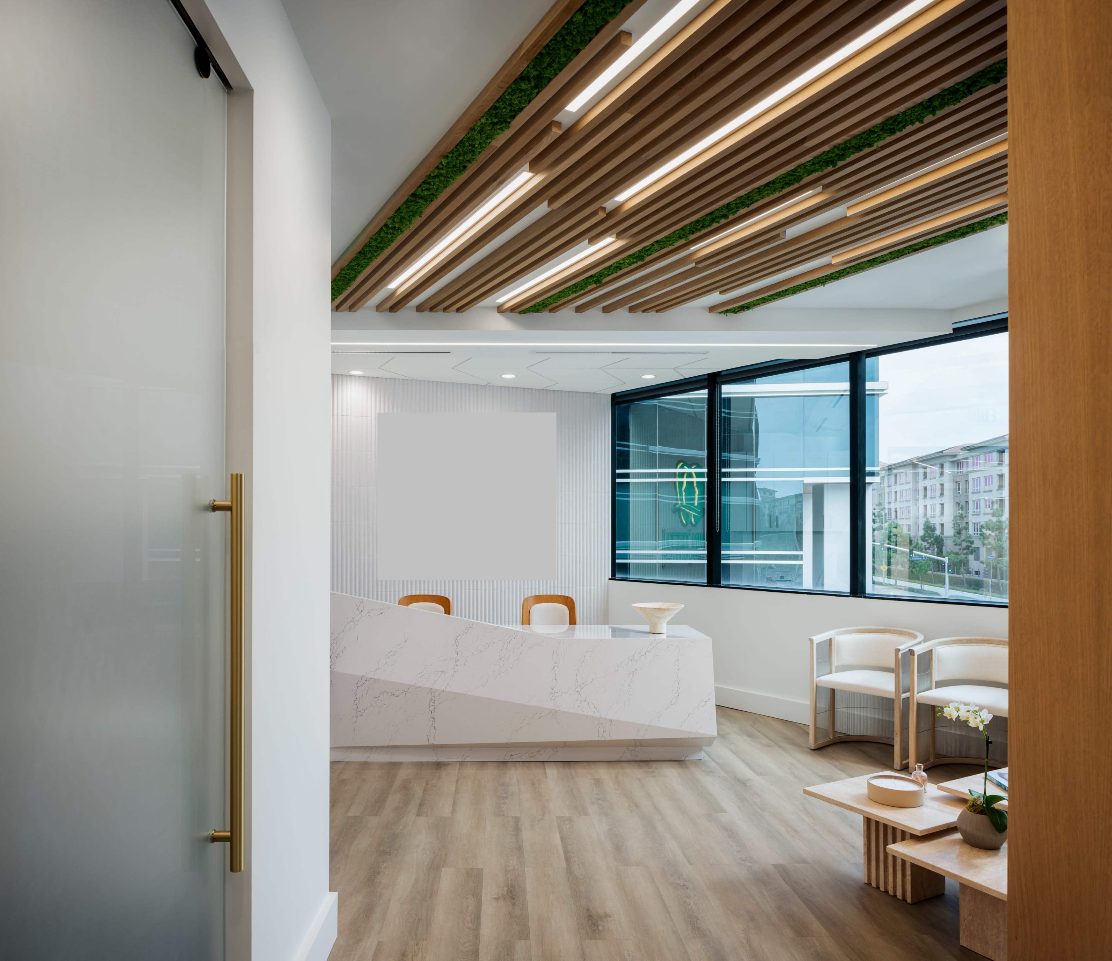 The image shows a modern reception area with a marble front desk, wooden ceiling beams, and large windows providing natural light.