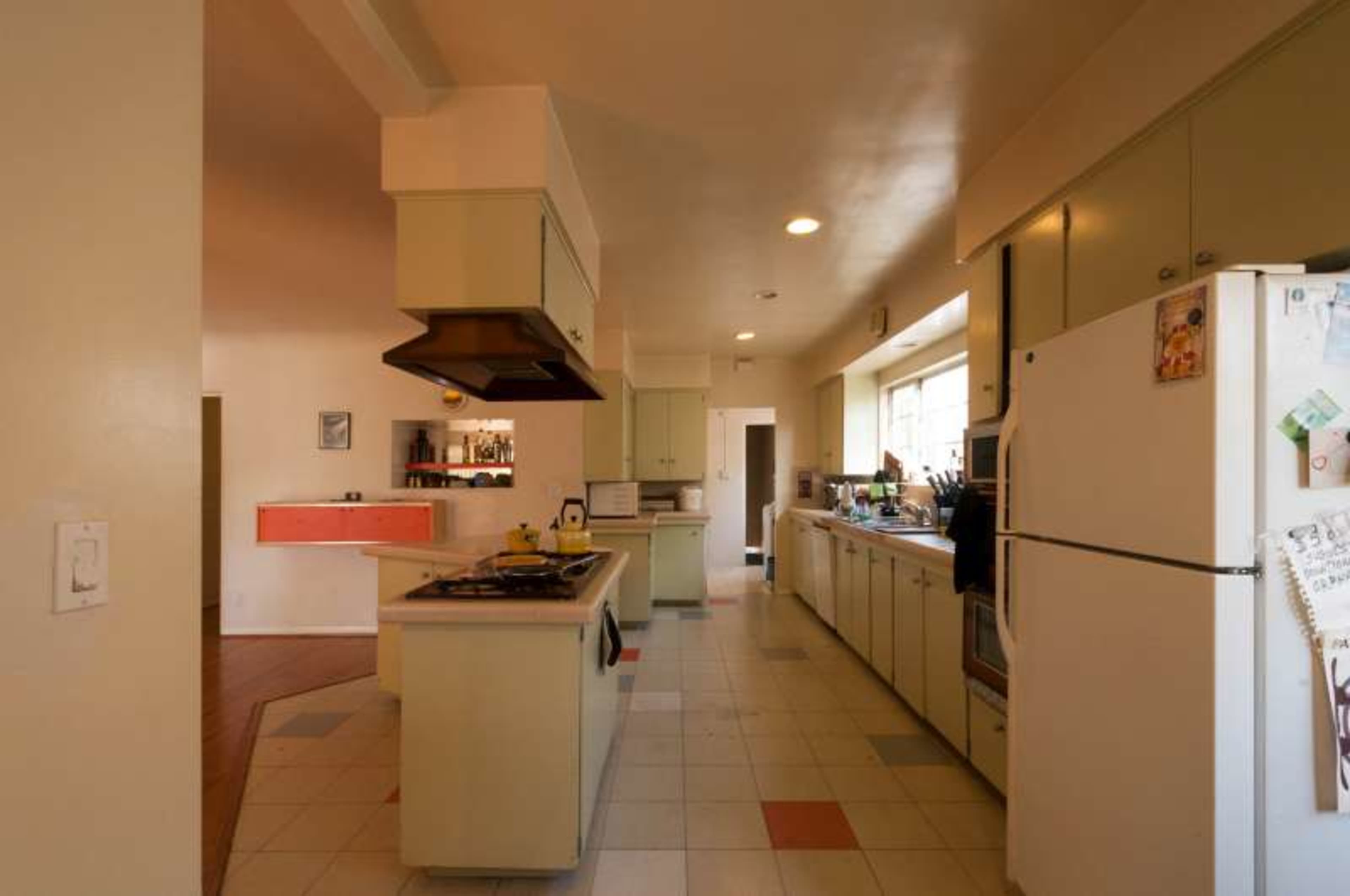 The image shows a spacious kitchen with light-colored cabinets, appliances, and a cooking area on the left side.