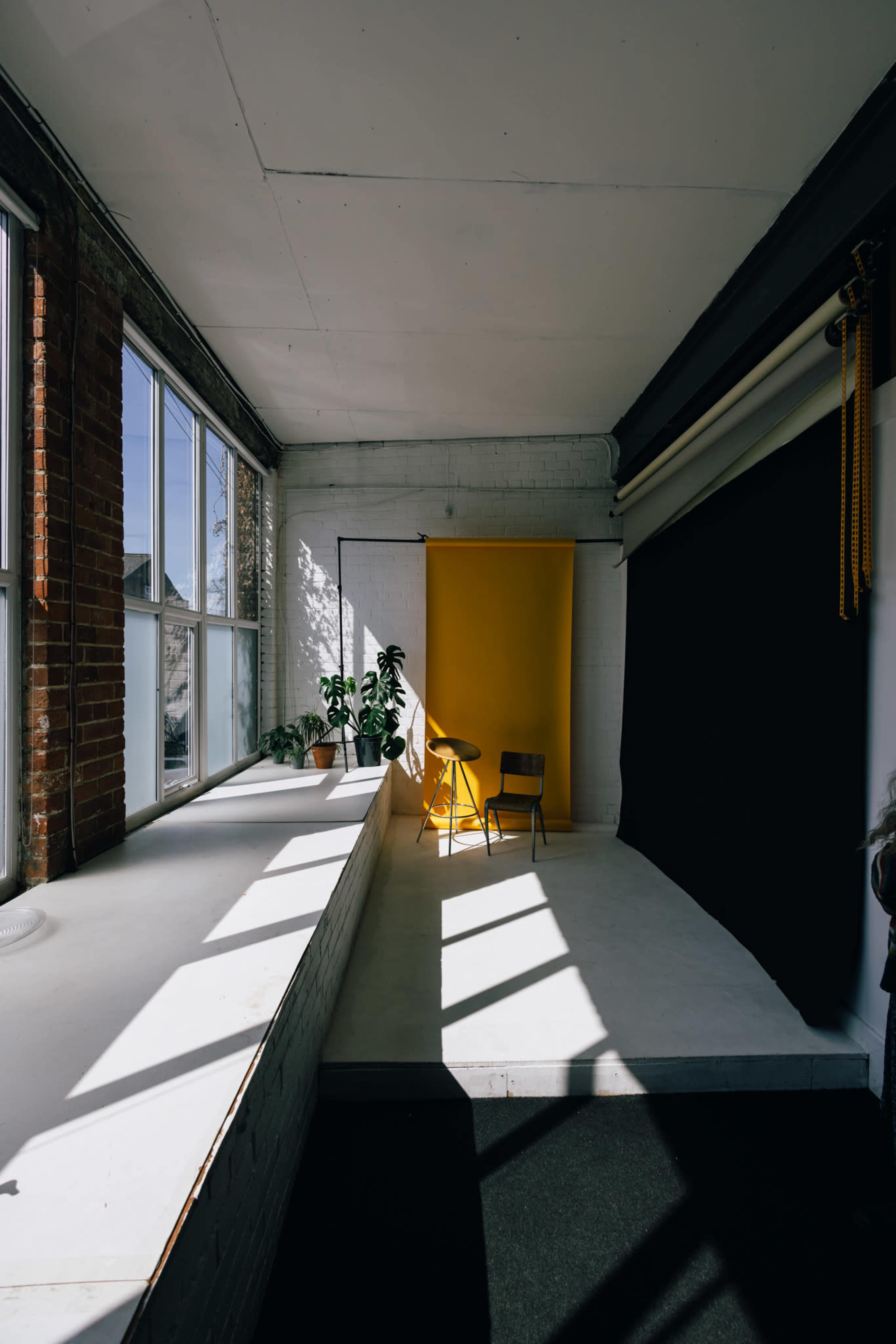 A spacious room with large windows, featuring a yellow backdrop, a chair, and a plant on a white countertop.