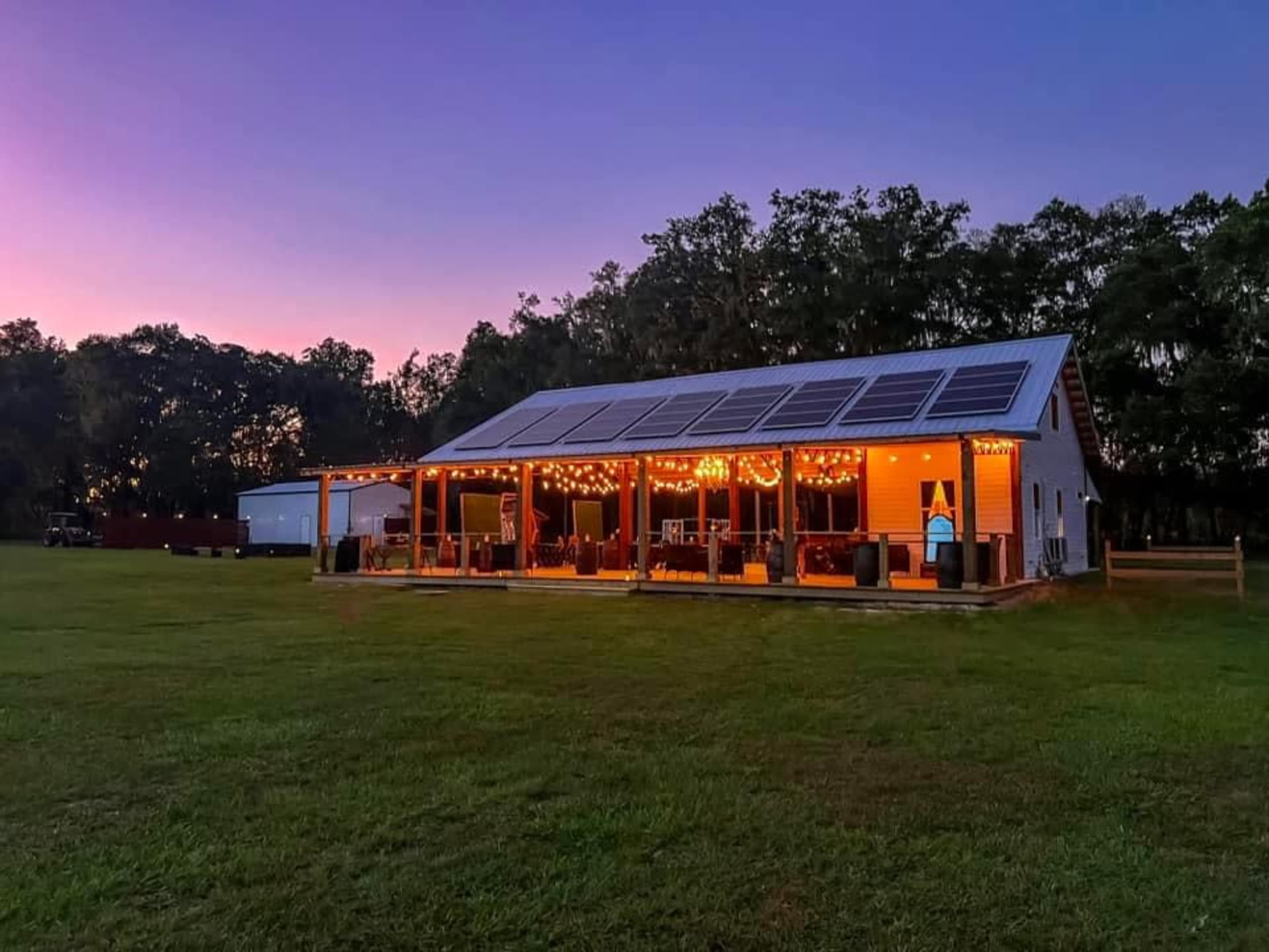 A modern house with solar panels on the roof is illuminated by string lights, set against a twilight sky.