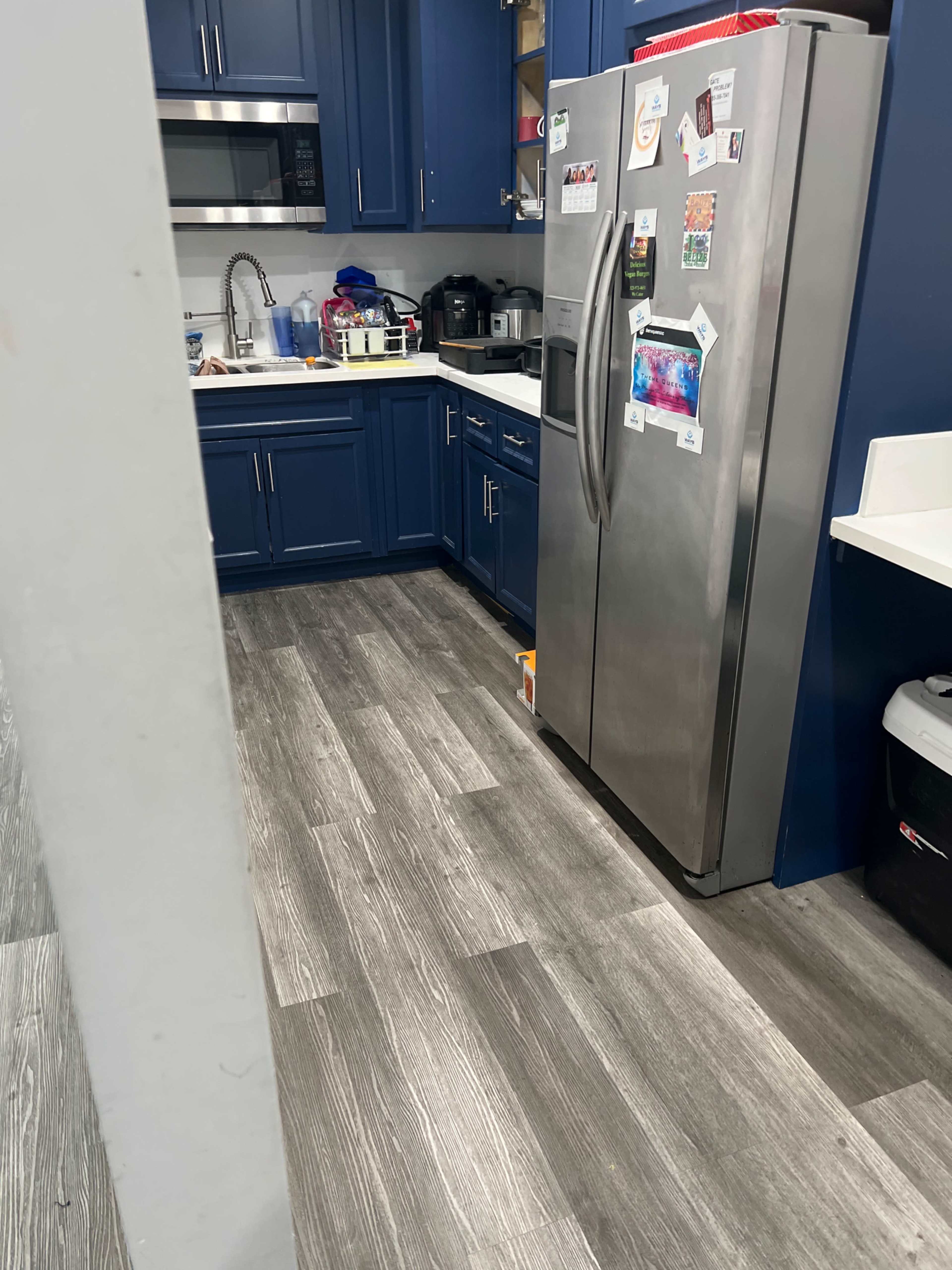 A kitchen with navy blue cabinets, stainless steel appliances, and a wooden floor.