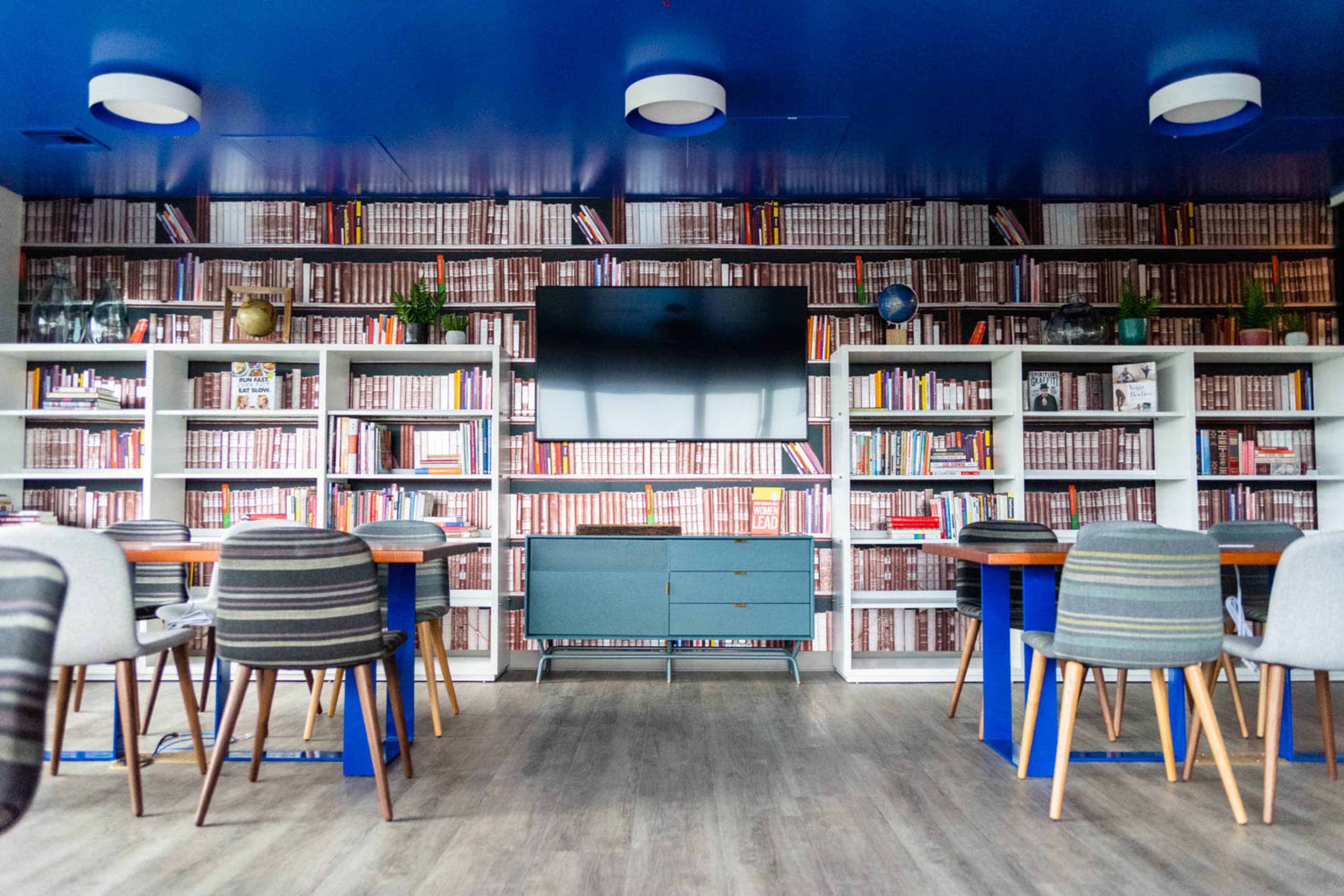 A modern room with shelves filled with books on the walls, a central television, and tables surrounded by chairs.