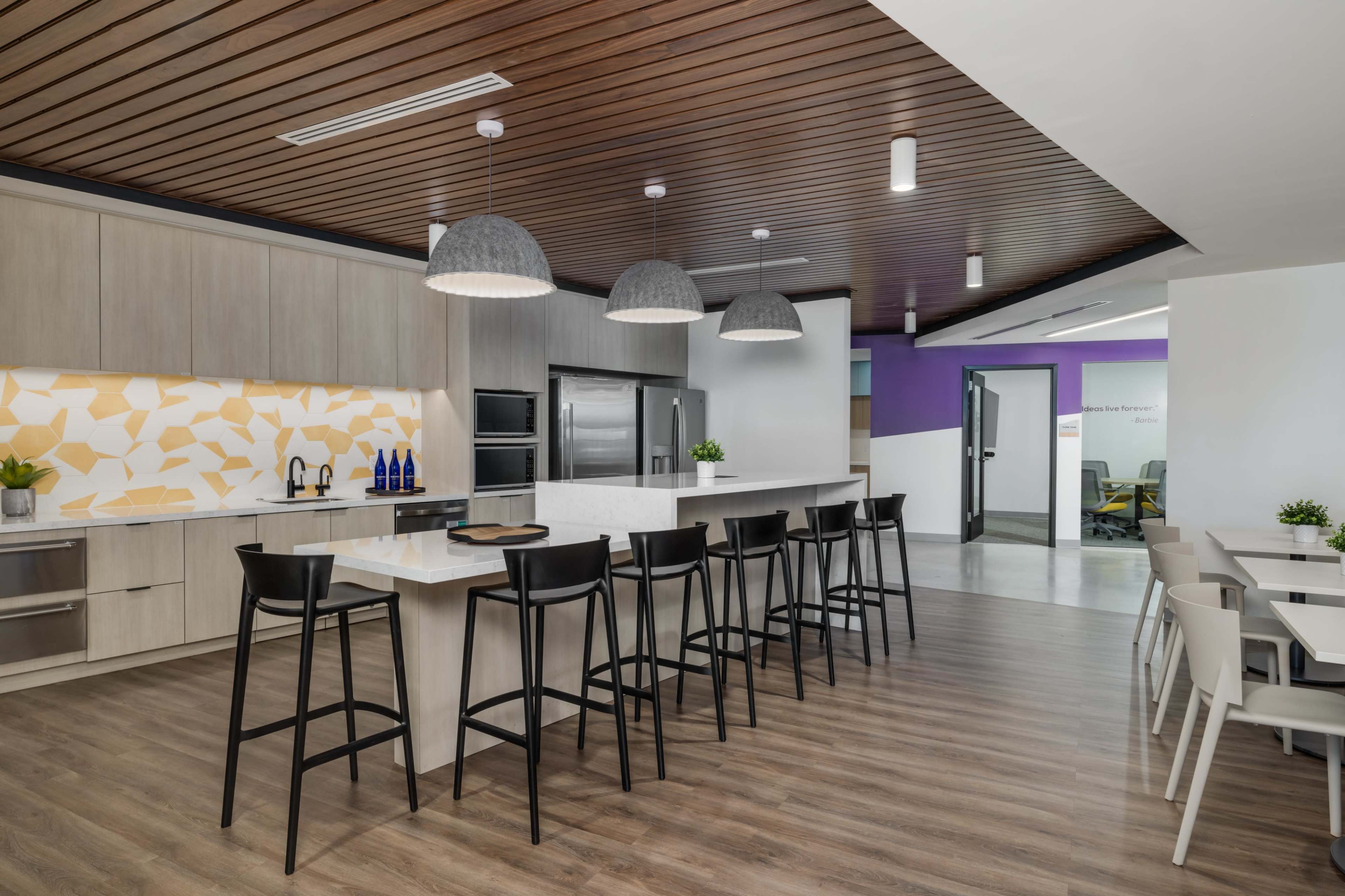 The image shows a modern kitchen area with a large island, bar stools, and contemporary appliances, featuring a geometric backsplash and pendant lighting.