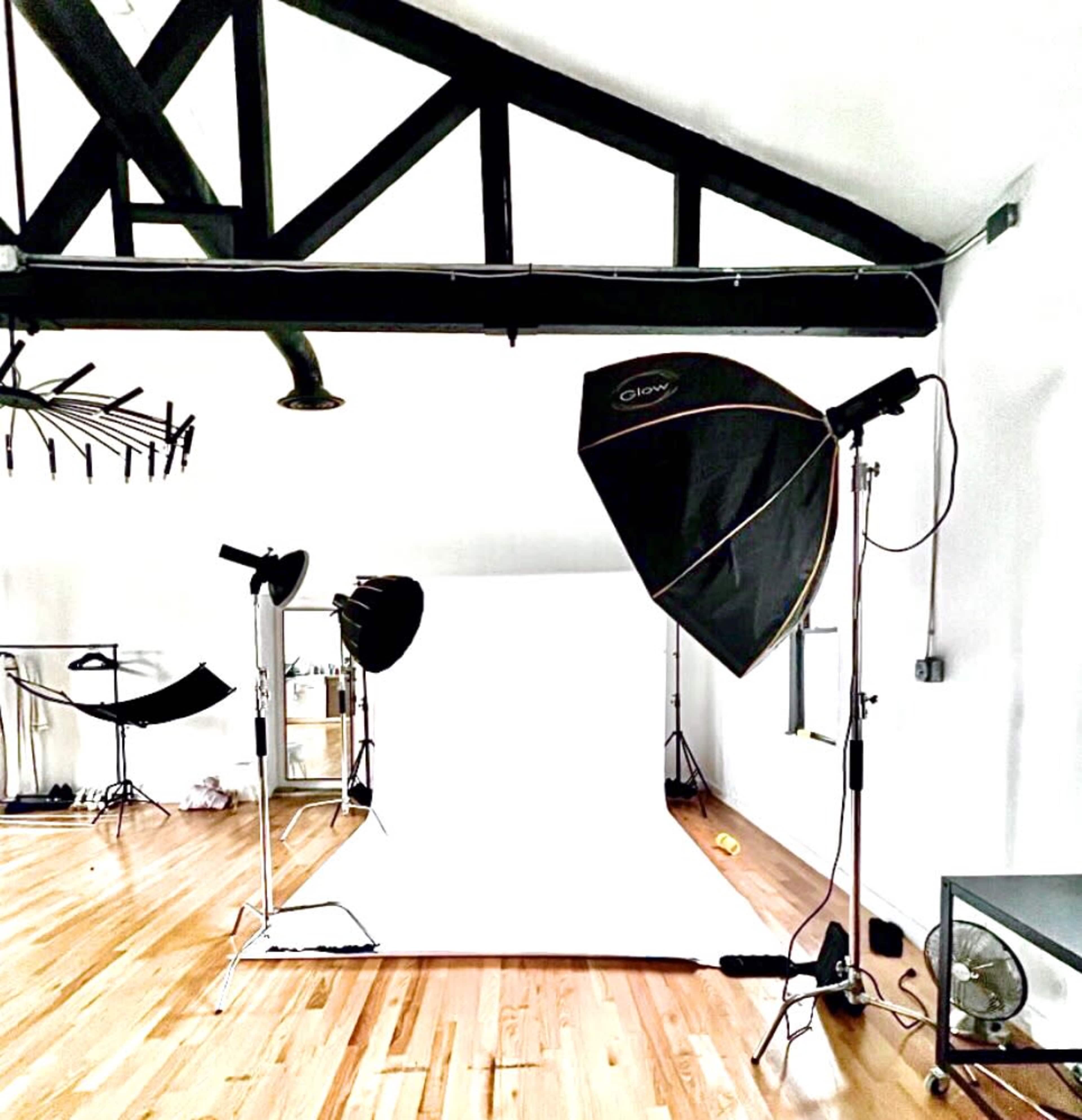 The image shows a photography studio with a blank white backdrop, lighting equipment, and wooden floors.
