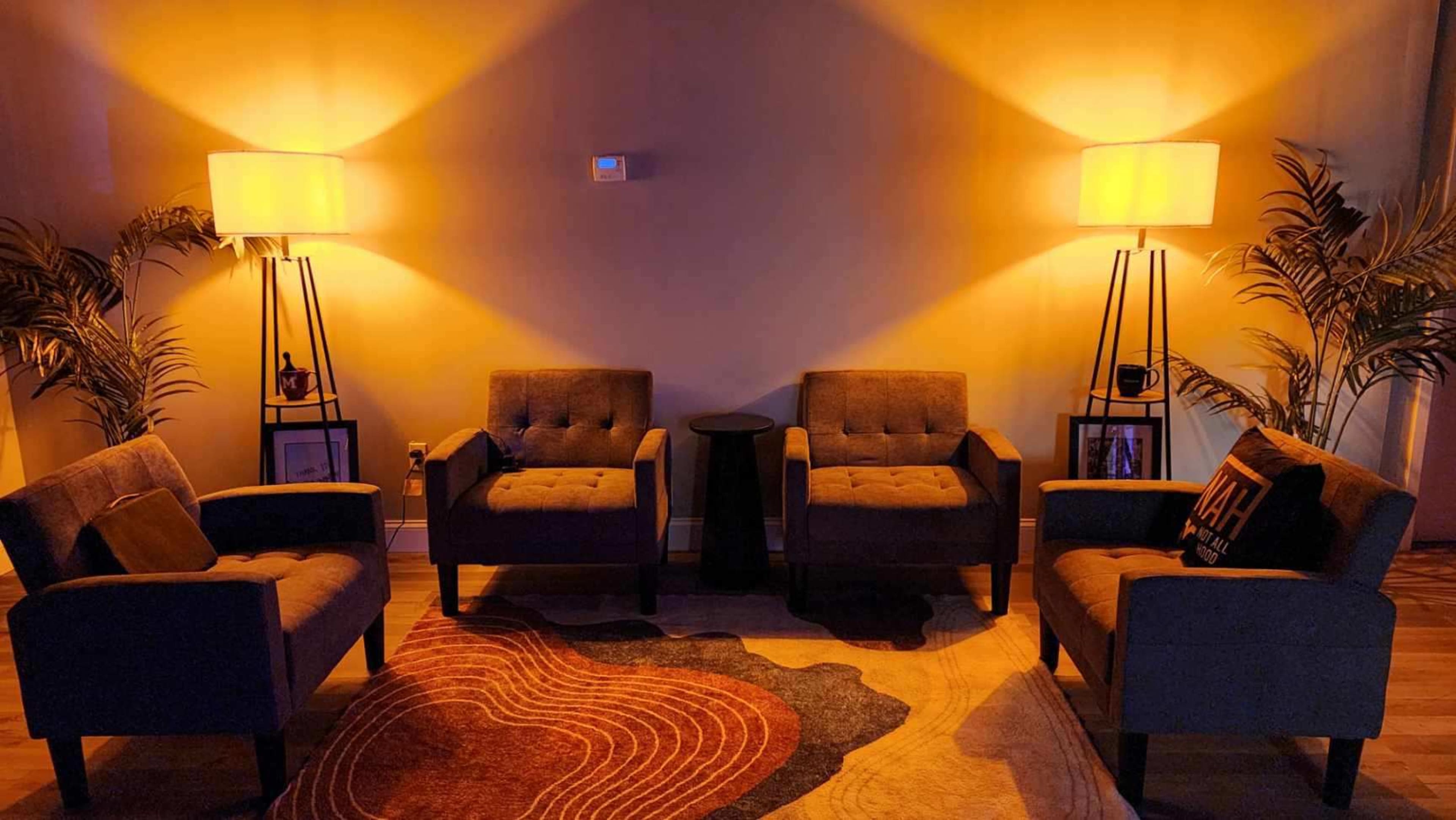 The image shows a cozy seating area with four upholstered chairs, a small side table, and a decorative rug under warm lighting.