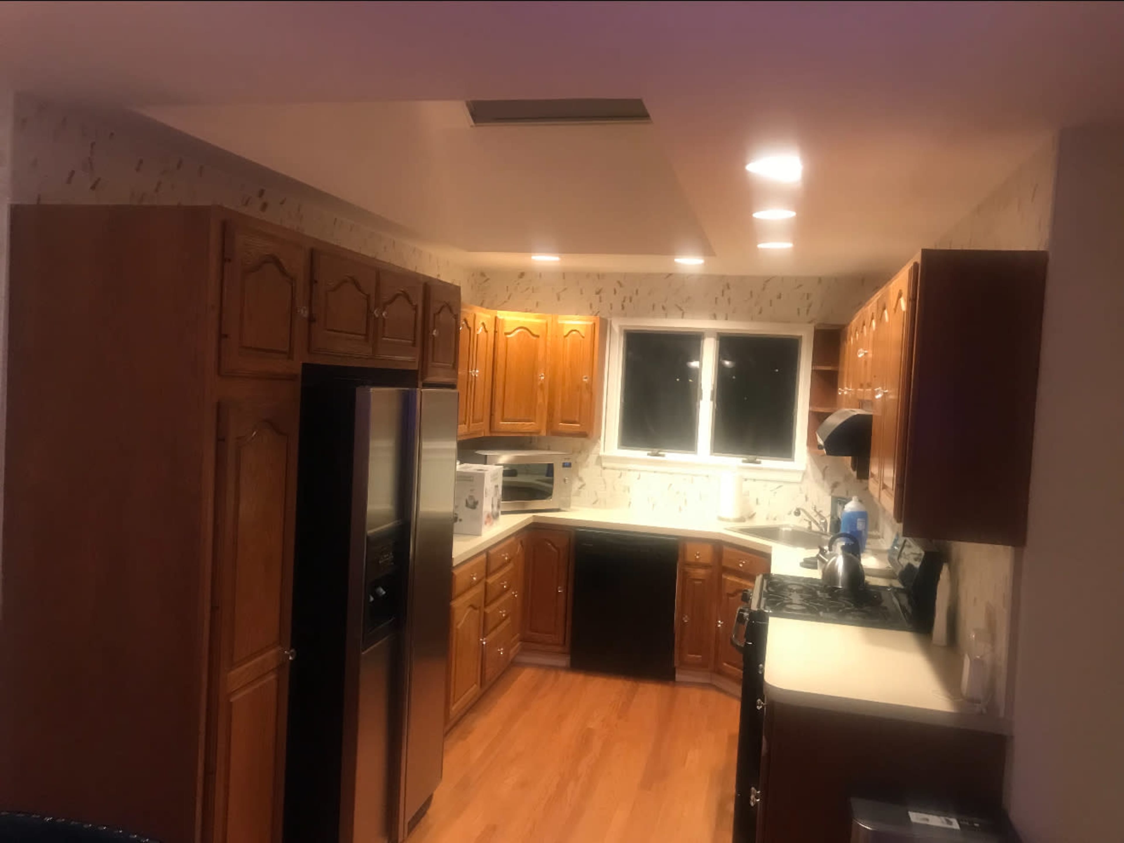 The image shows a kitchen with wooden cabinetry, appliances including a refrigerator and stove, and a window above the sink.