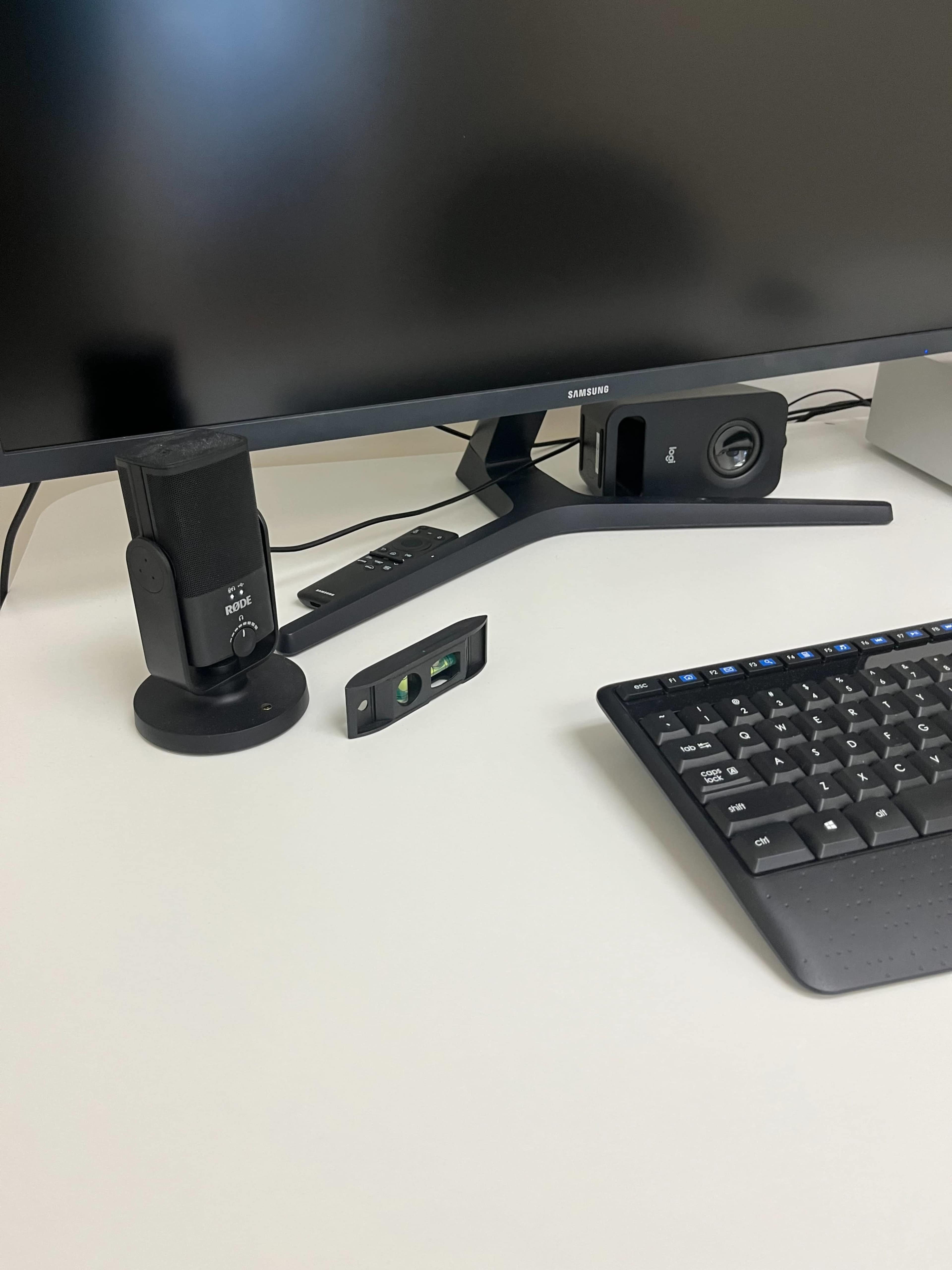 The image shows a workspace with a monitor, a microphone on a stand, a small device, a keyboard, and a speaker.