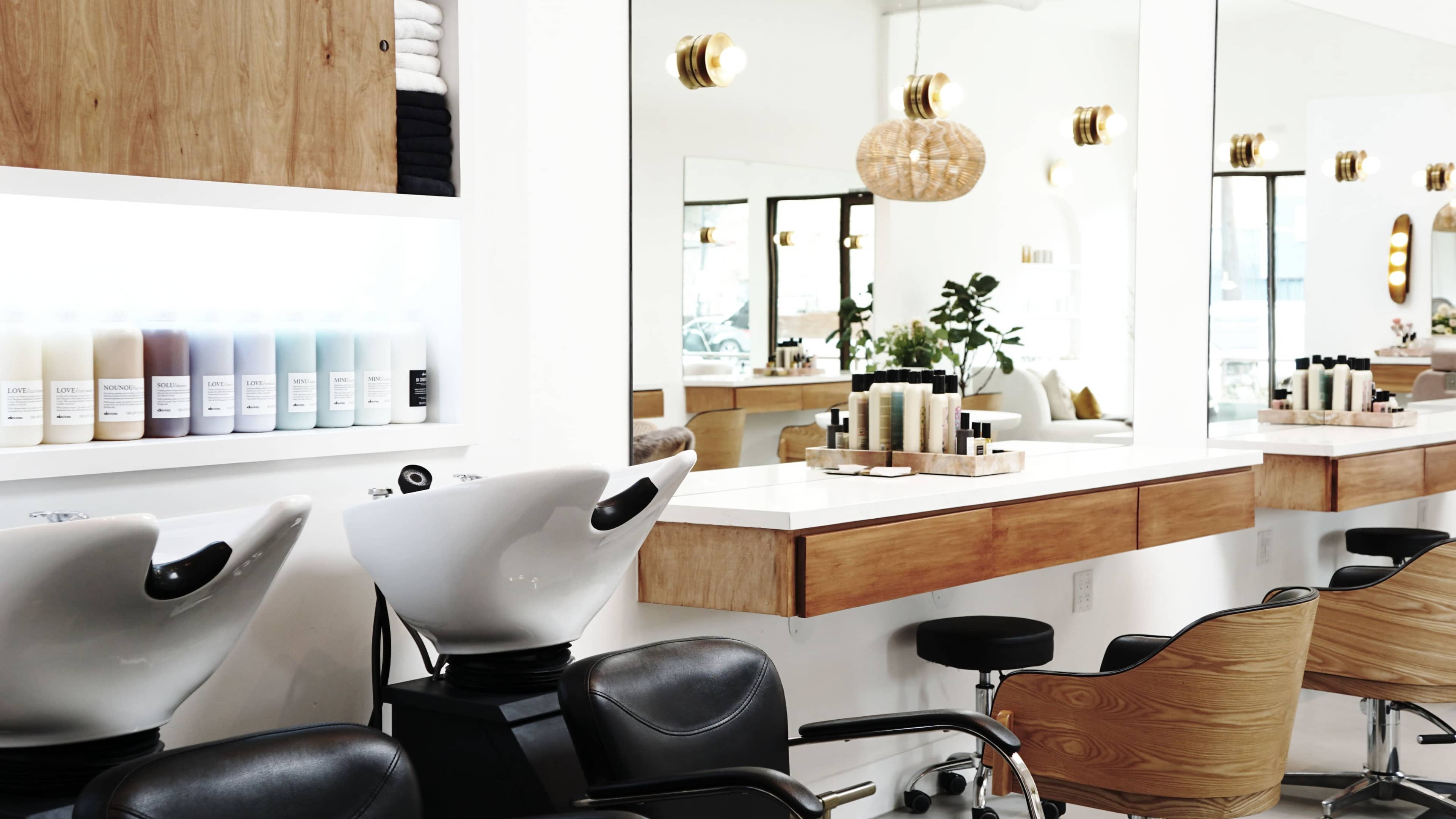 The image shows a modern hair salon with two shampoo stations, wooden accents, and a large mirror reflecting the interior.