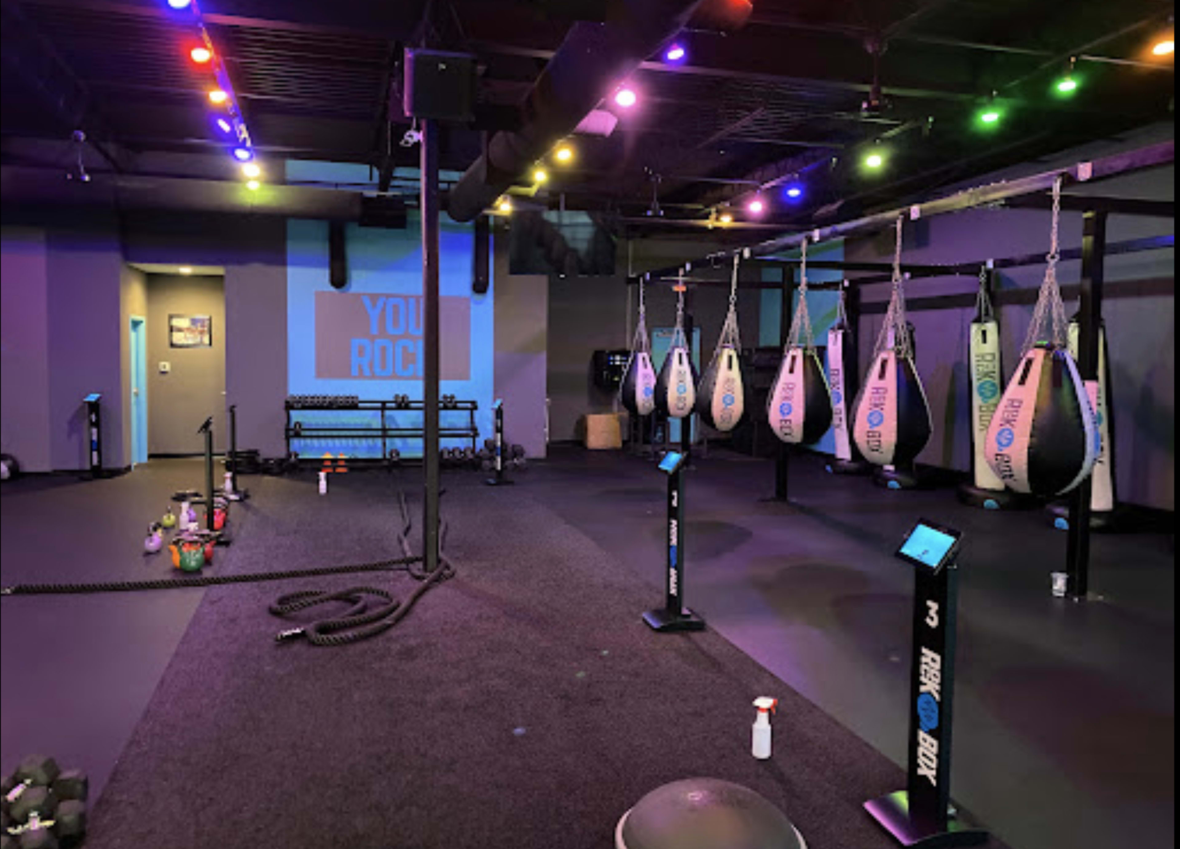 A fitness studio equipped with several punching bags, exercise equipment, and colorful overhead lights.