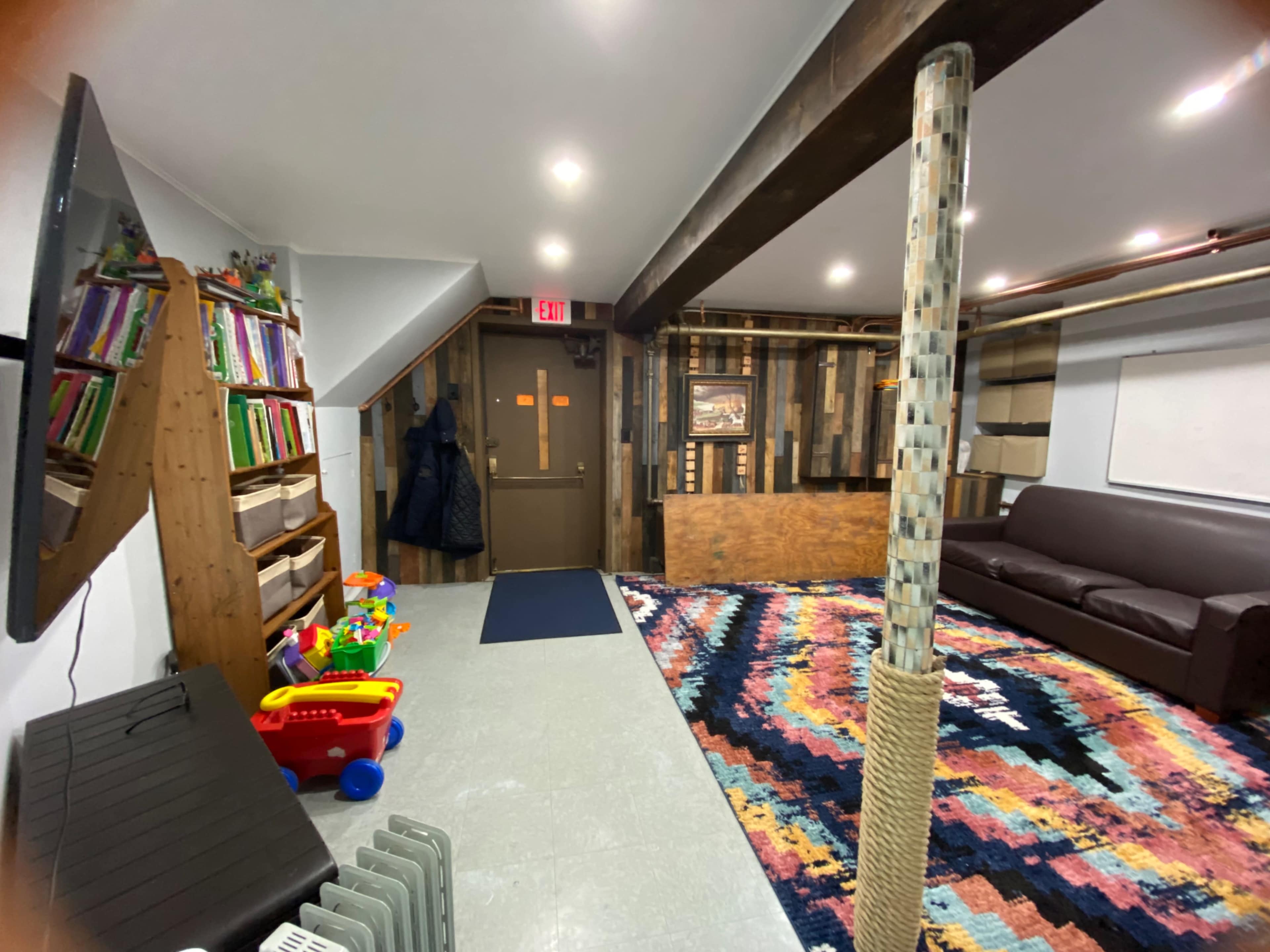 A multifunctional basement features a carpet, a couch, storage shelves, and a colorful play area with children's toys.