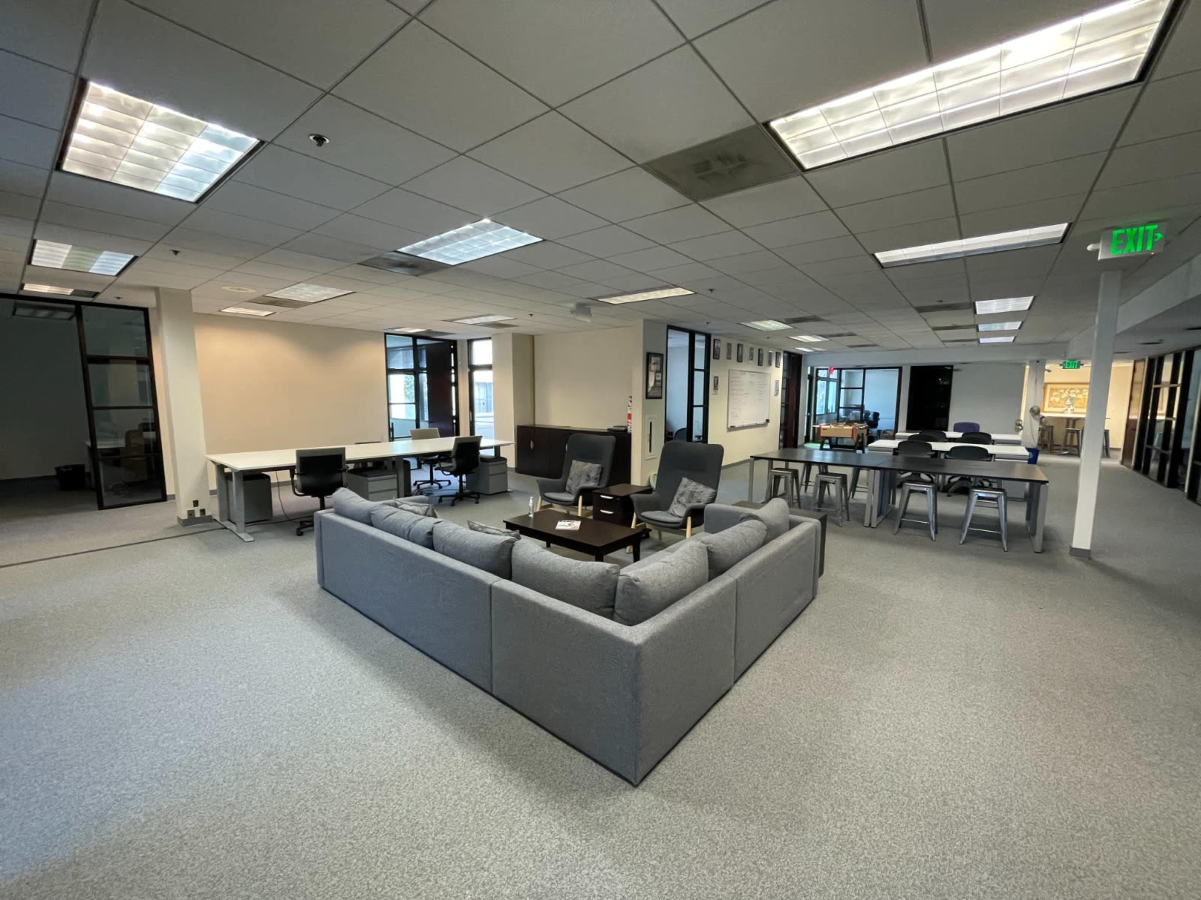 A spacious office area with a gray sectional couch in the center, surrounded by tables and chairs.