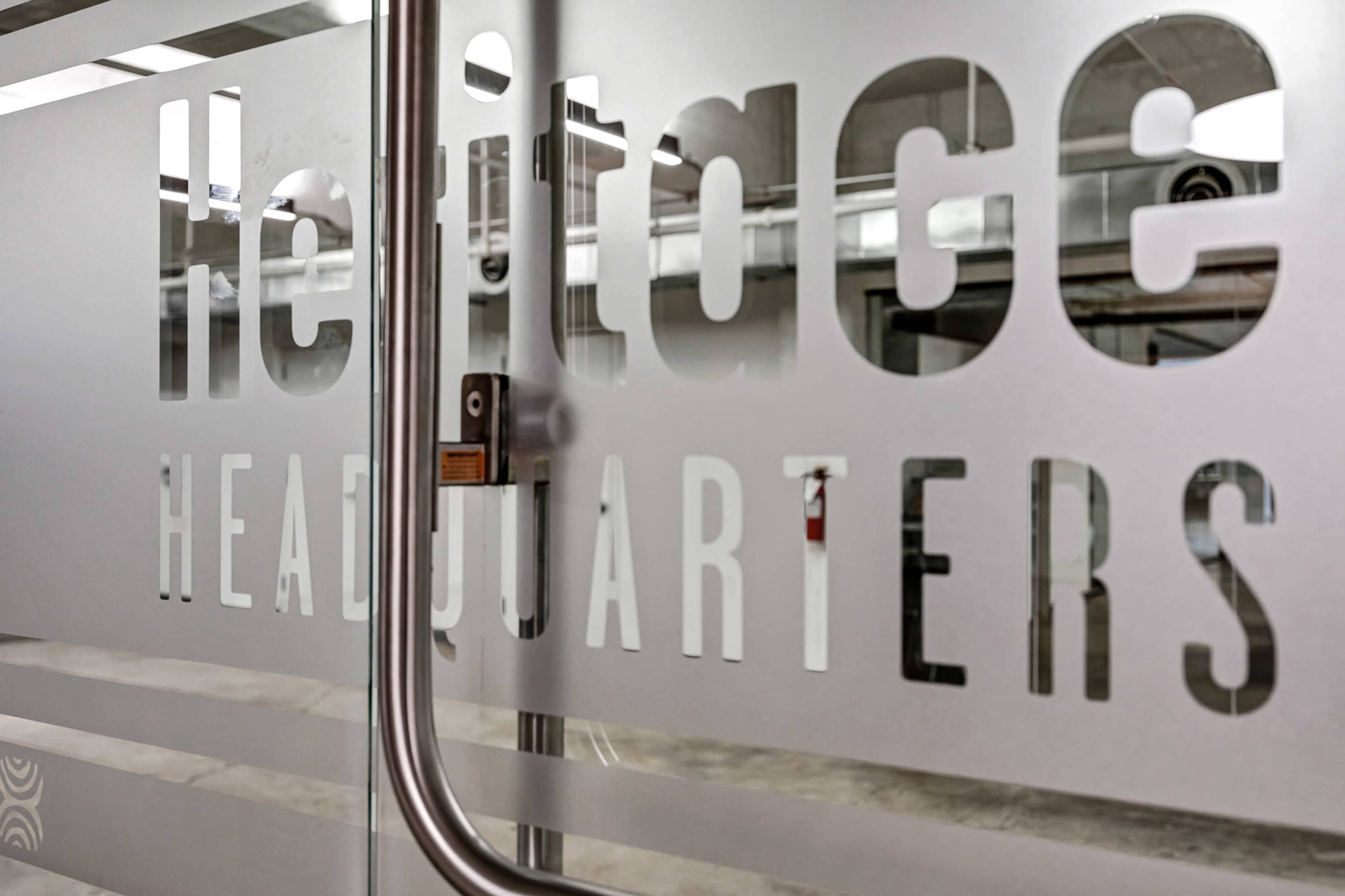 The image shows a glass door with the words "Heritage HEADQUARTERS" etched into the surface.