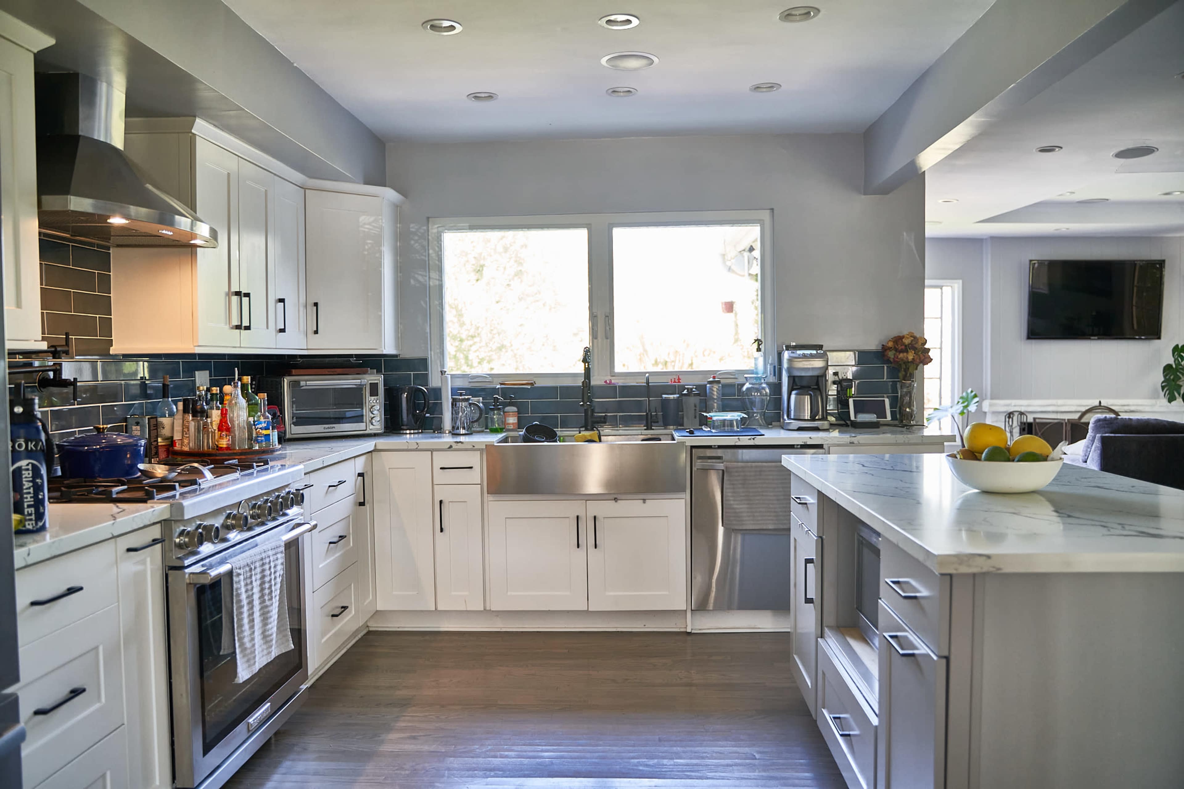 A modern kitchen features white cabinets, a stainless steel stove, and a large window overlooking a well-lit area.