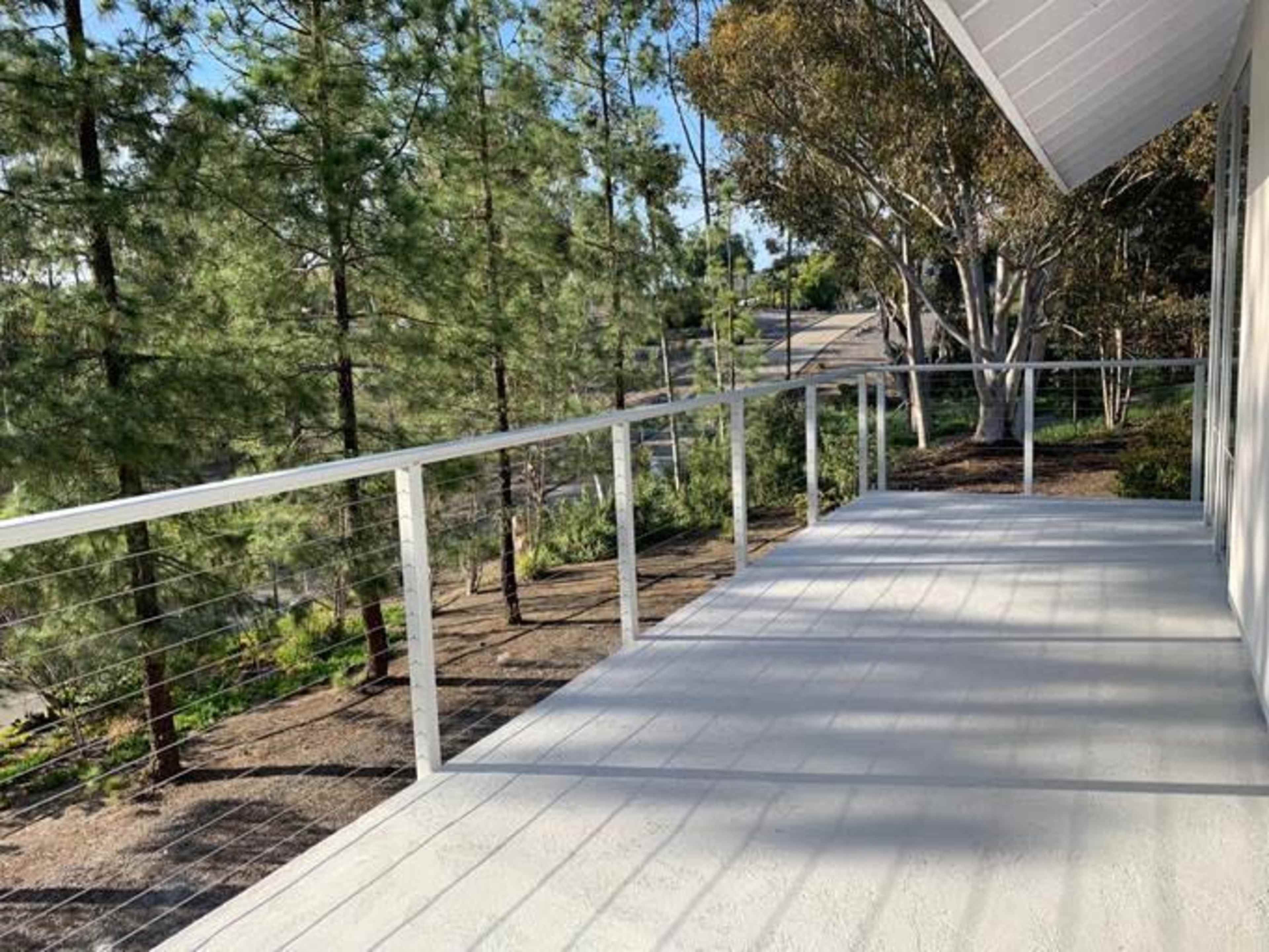 The image shows a deck with a white railing surrounded by trees and a pathway in the background.