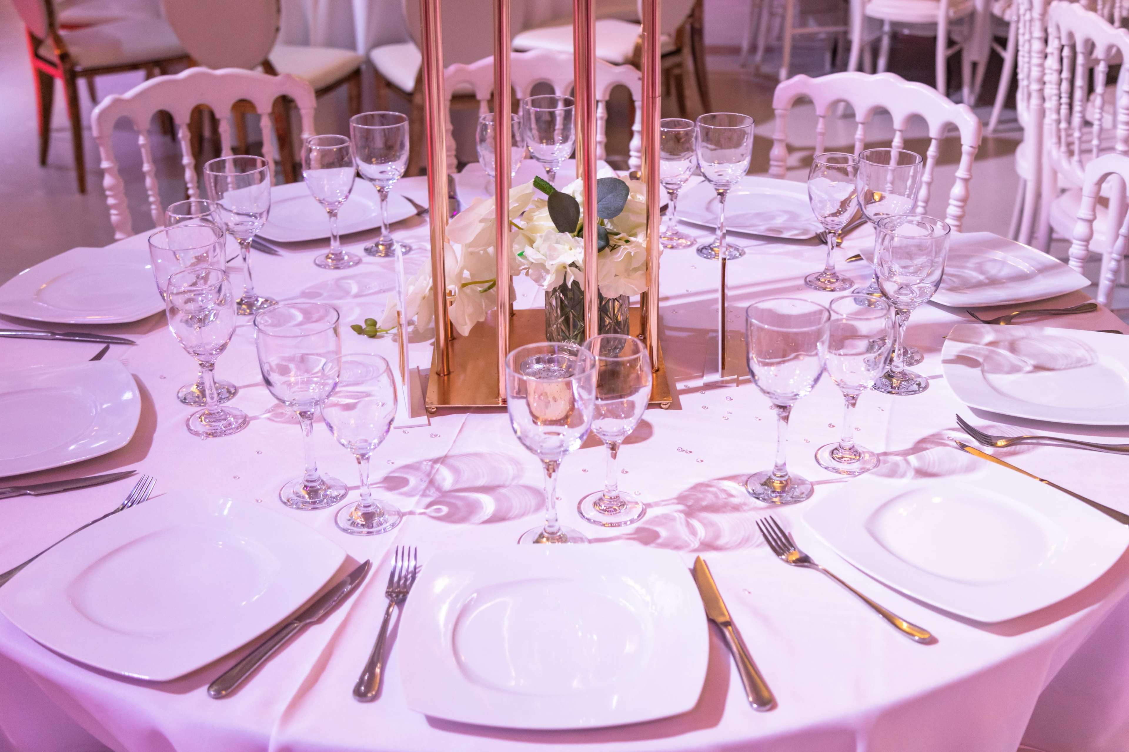 A round table set for a formal event features white plates, crystal glassware, and a floral centerpiece.