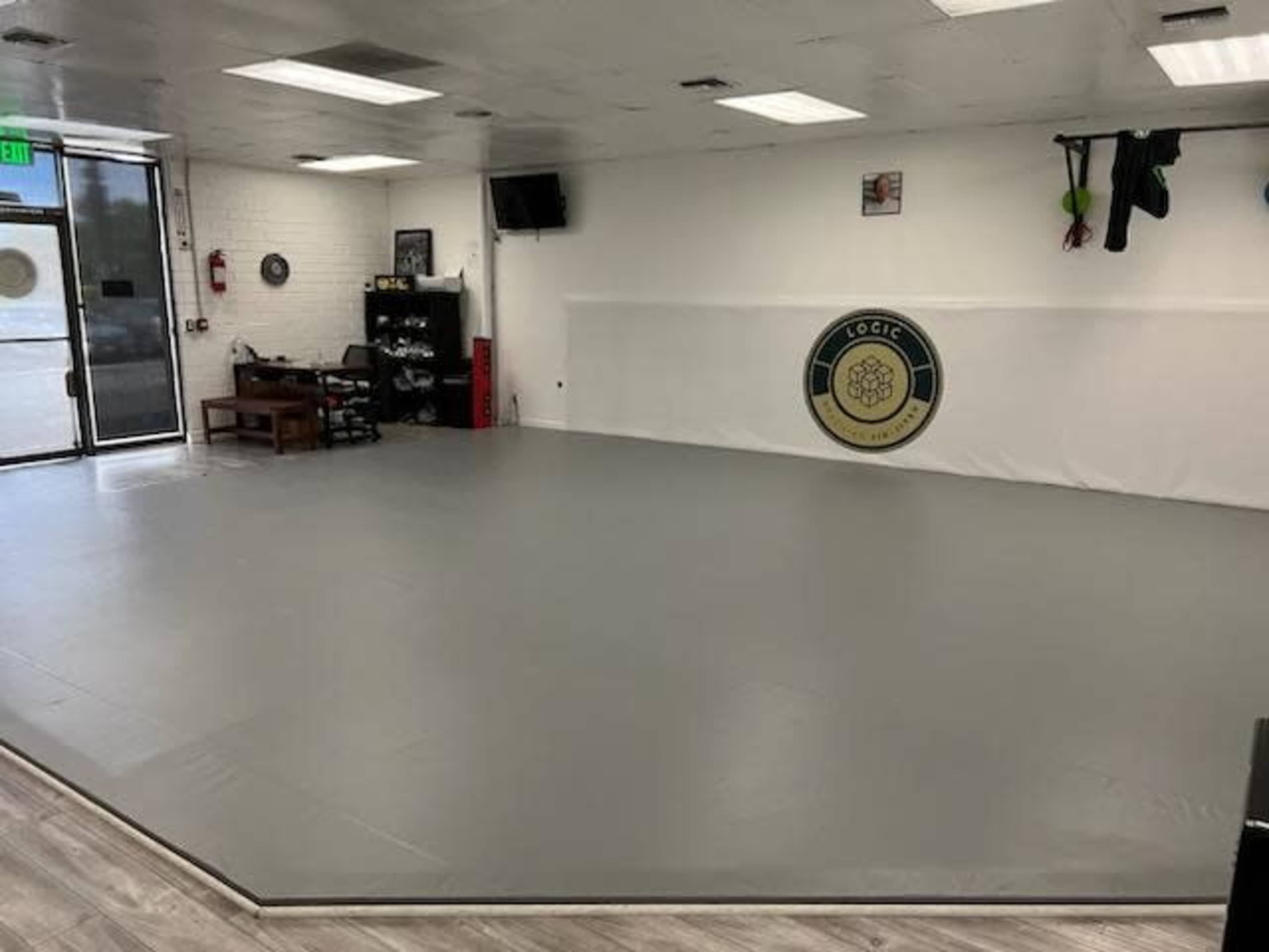 An empty martial arts studio with a gray mat, a wall logo, and a large entrance area.