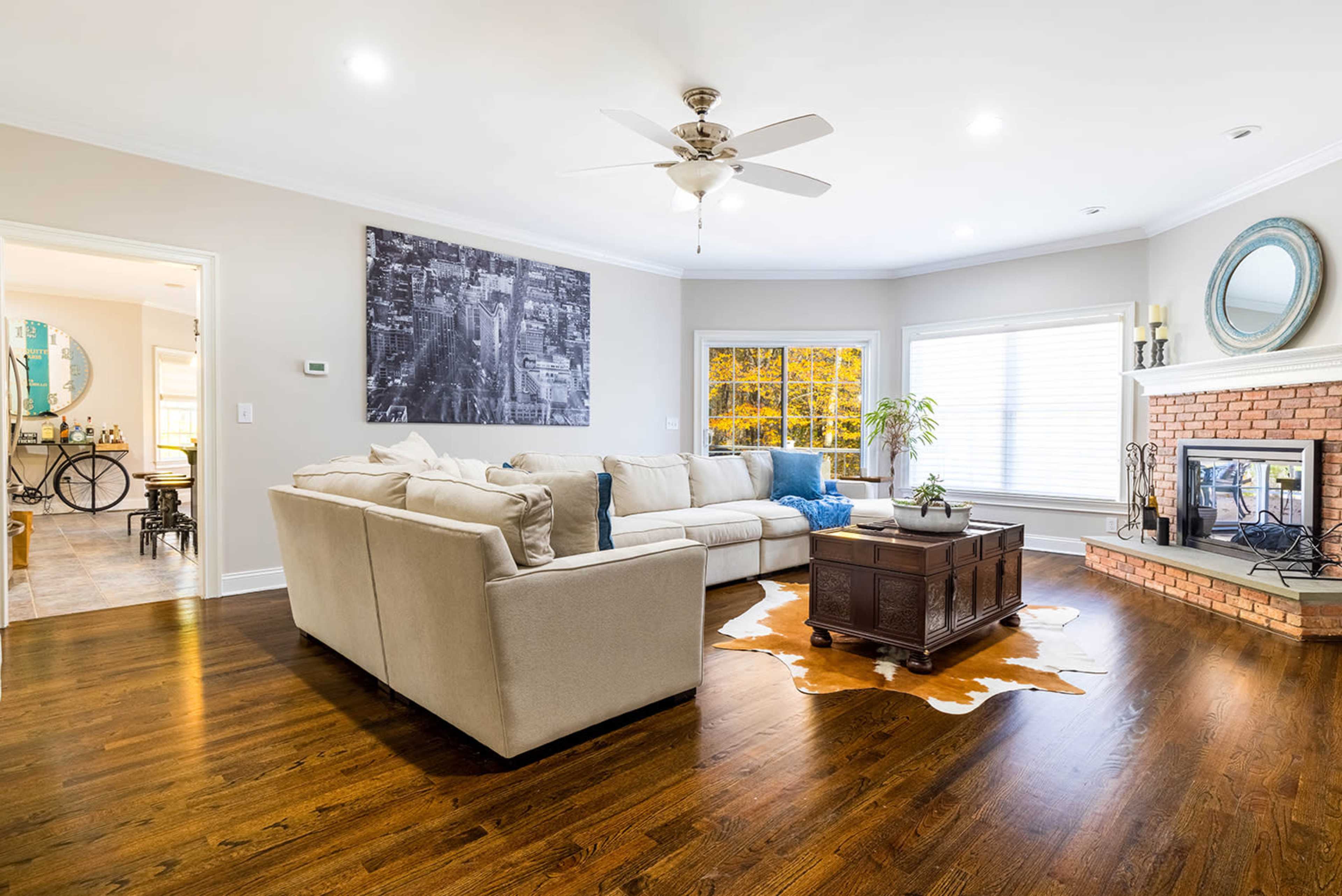 A spacious living room features a large sectional sofa, a coffee table on a cowhide rug, and a fireplace with a decorative mirror above it.
