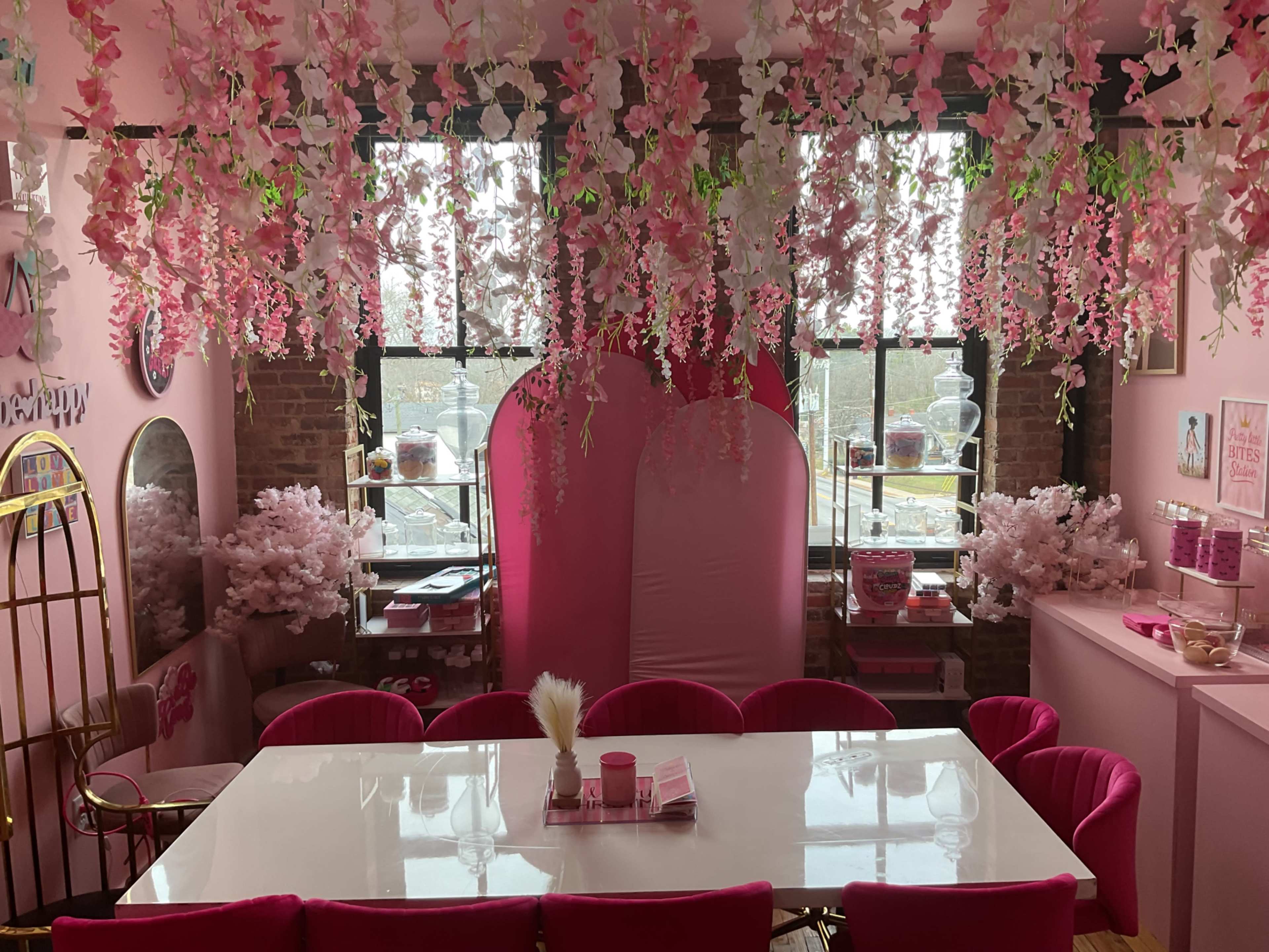 The room features pink decor with floral hanging arrangements, a white table, and various pink accessories throughout.