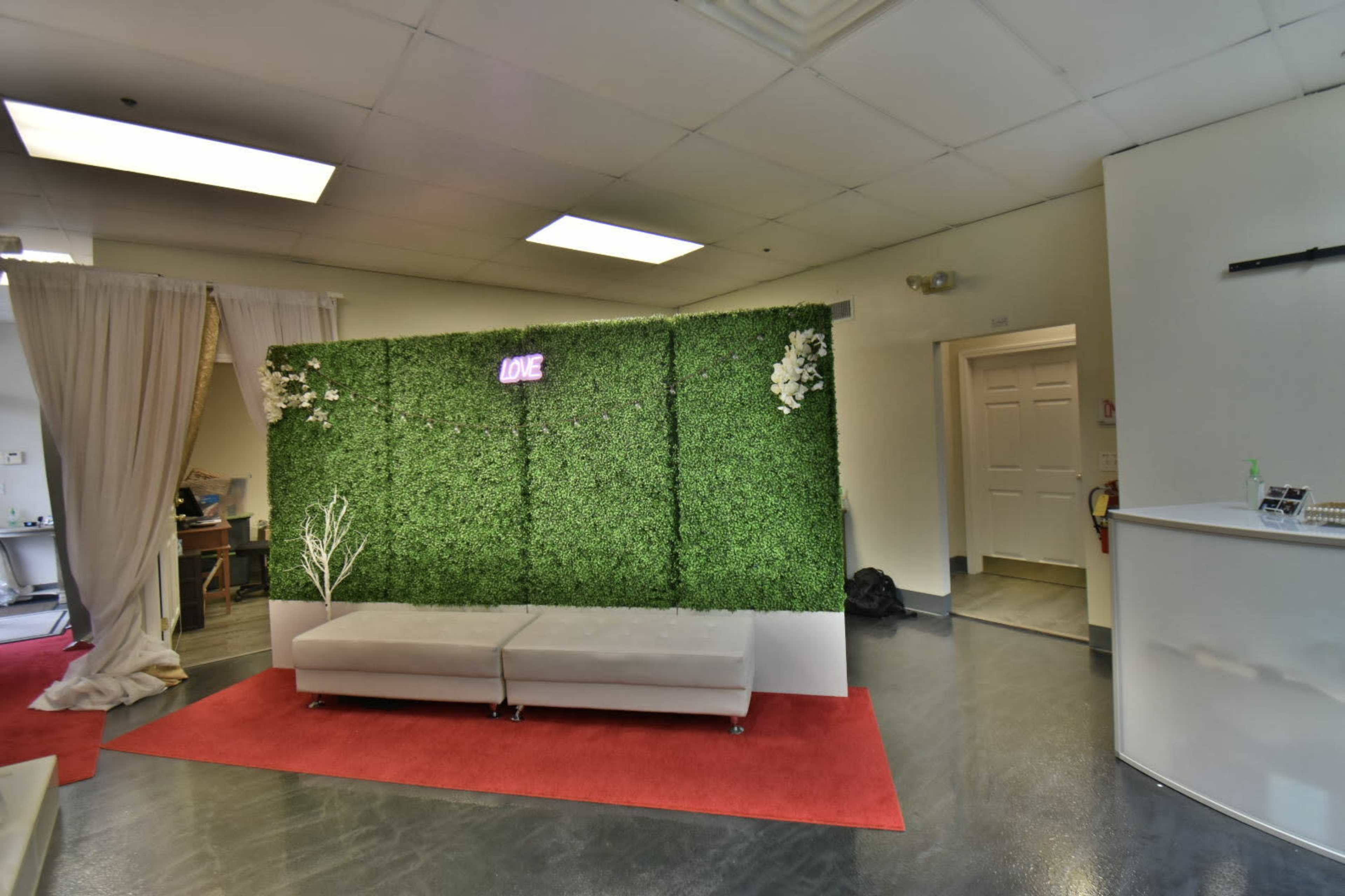 The image shows a small interior space featuring a green moss wall with the word "LOVE" illuminated, a gray sofa, and a red carpet.