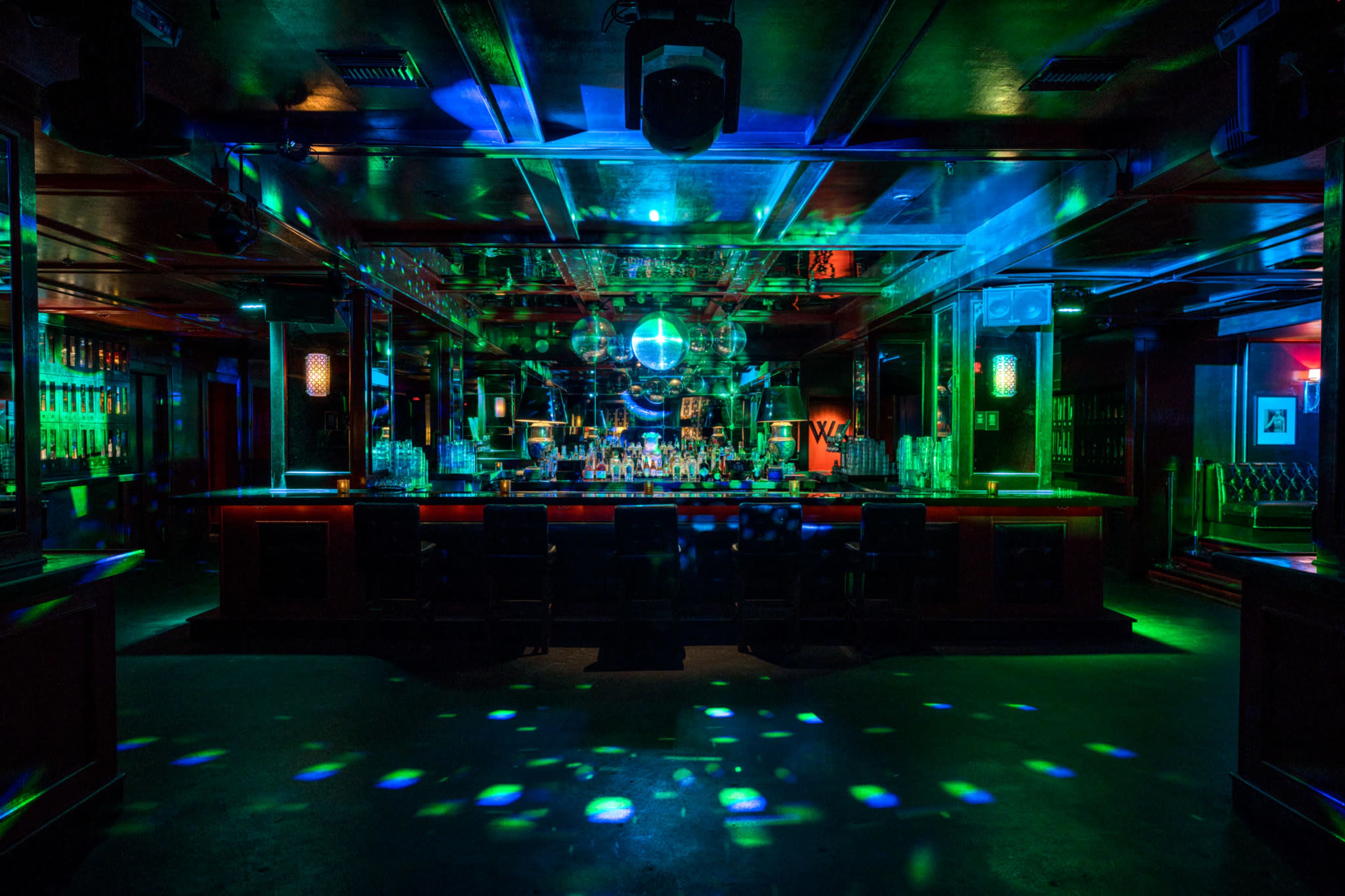 The image shows a dimly lit bar area with colorful lights and a mirrored disco ball reflecting multiple patterns on the floor.