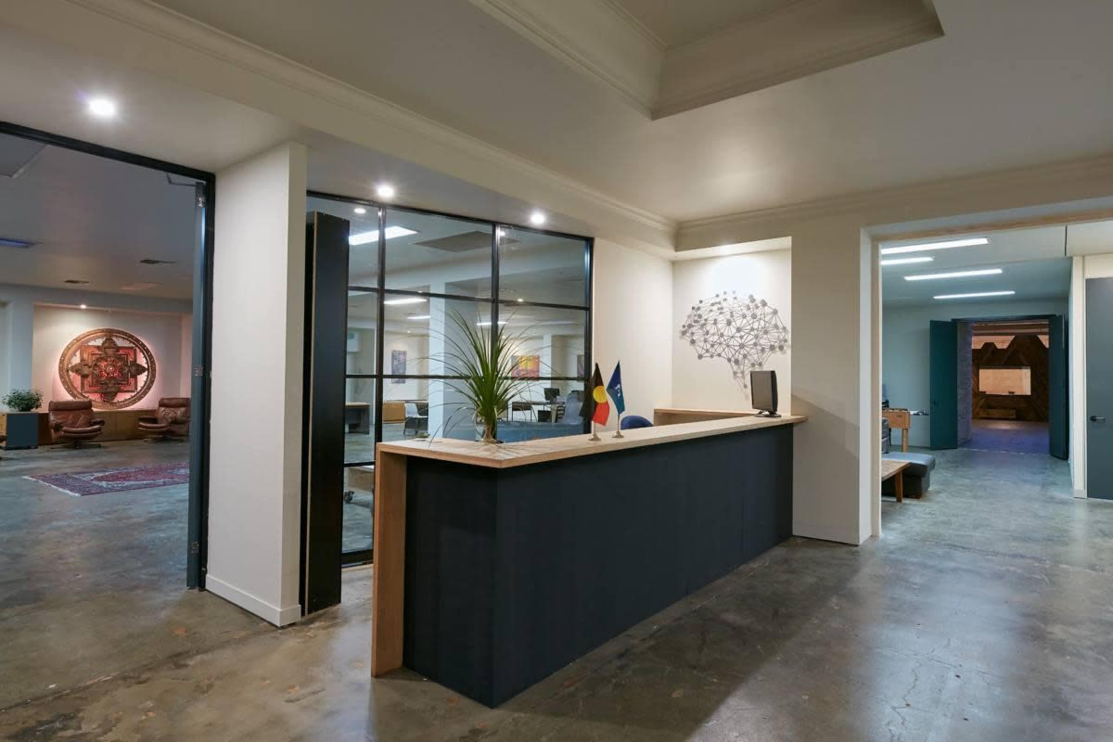 A modern reception area with a wooden desk, plants, and a glass partition leading to an office space.