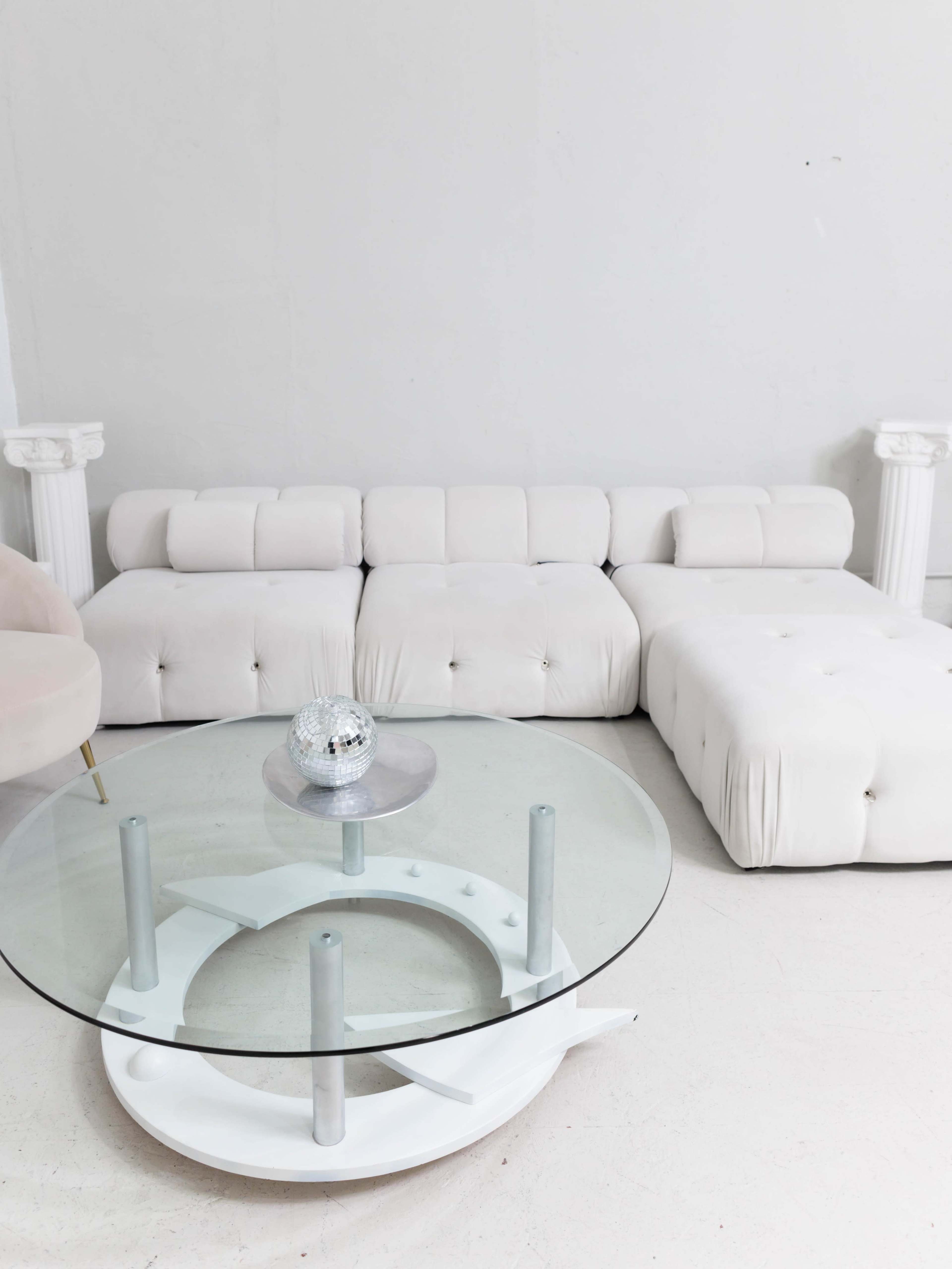A modern, white sectional sofa next to a round glass coffee table with a decorative disco ball on top.