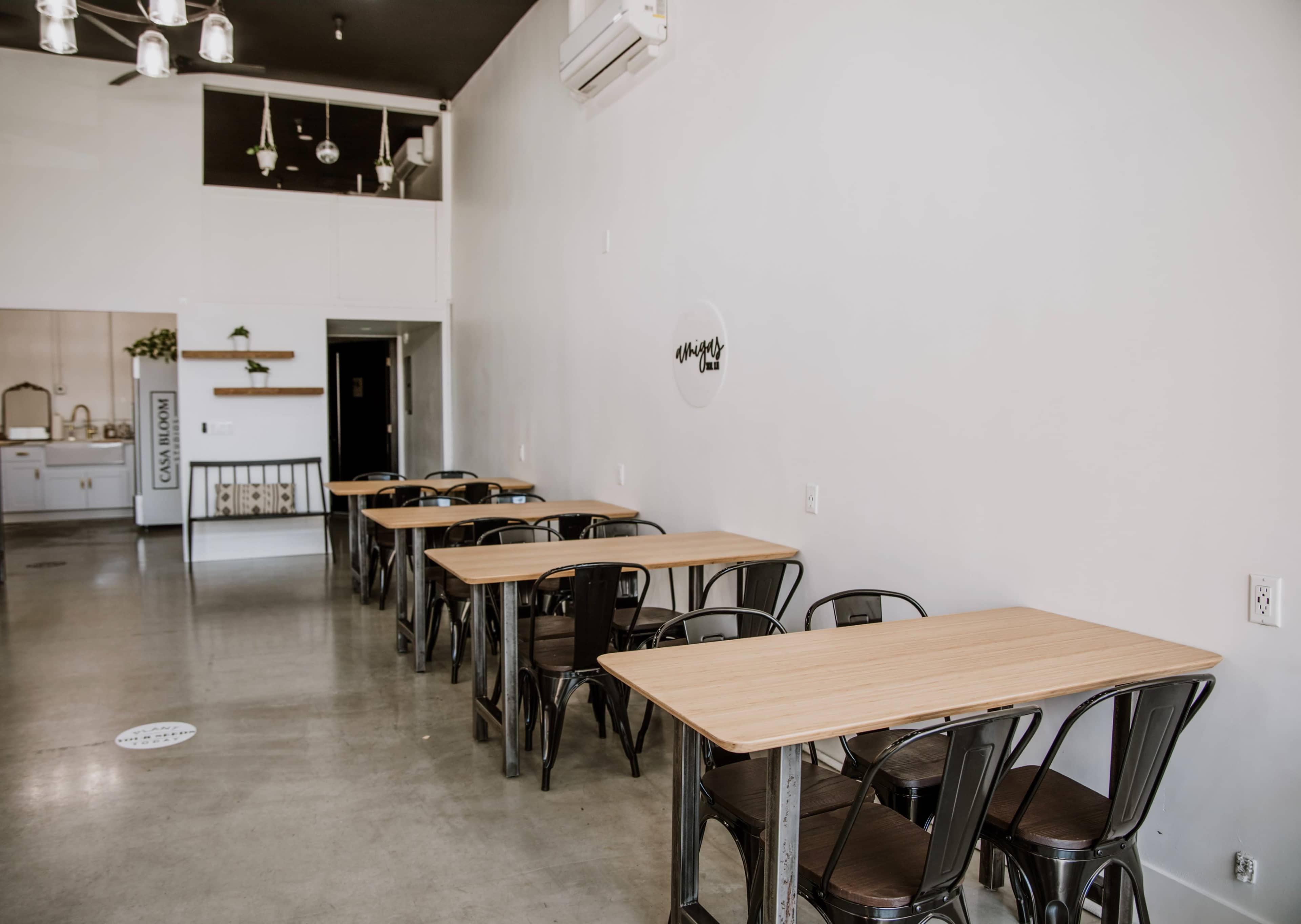 A minimalist café interior featuring several wooden tables and metal chairs arranged neatly in a spacious room with white walls.