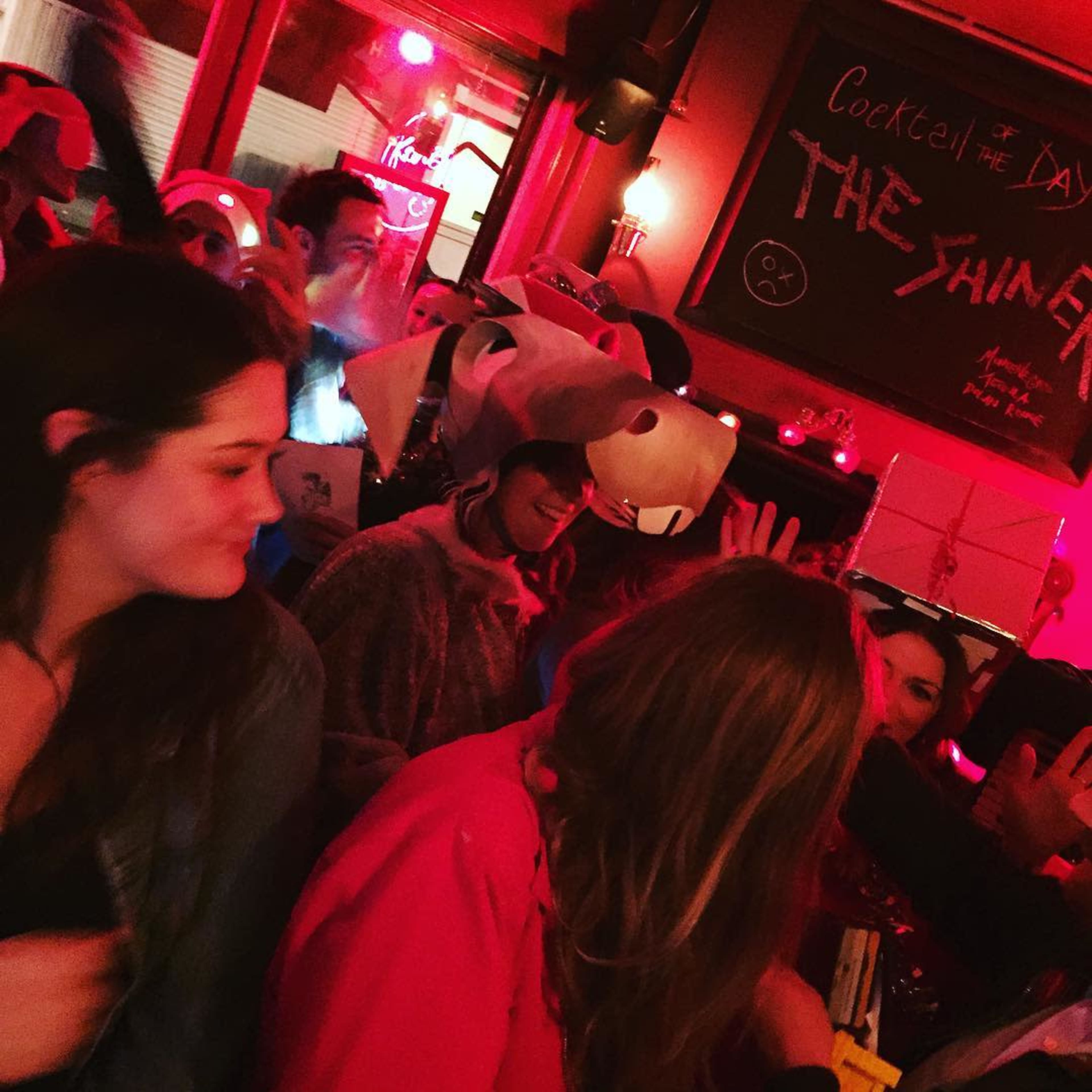A lively bar scene filled with people wearing various costumes under red lighting.